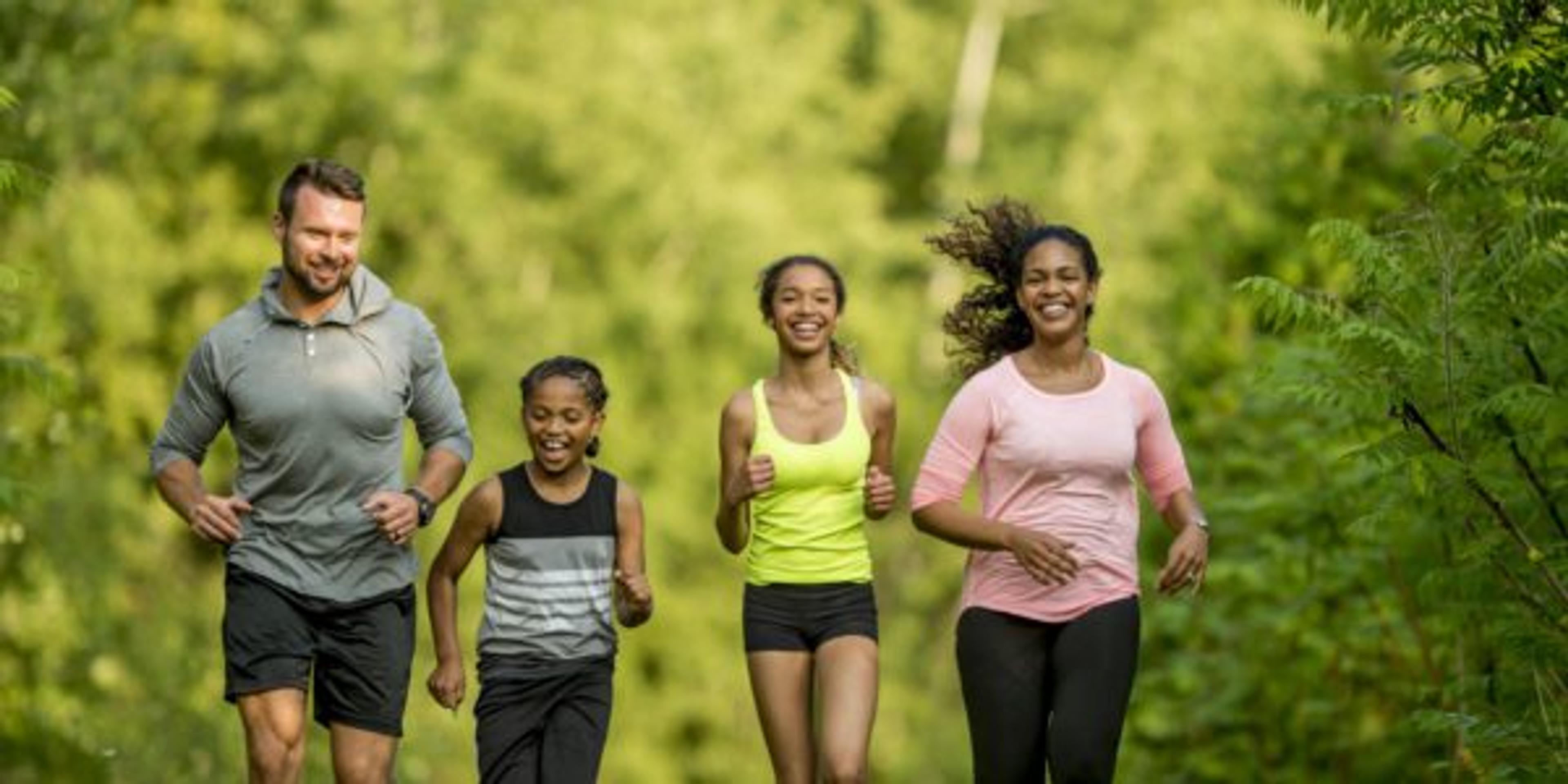 A multi-ethnic family (mother, father, son, daughter) getting exercise by going for a jog at the park.