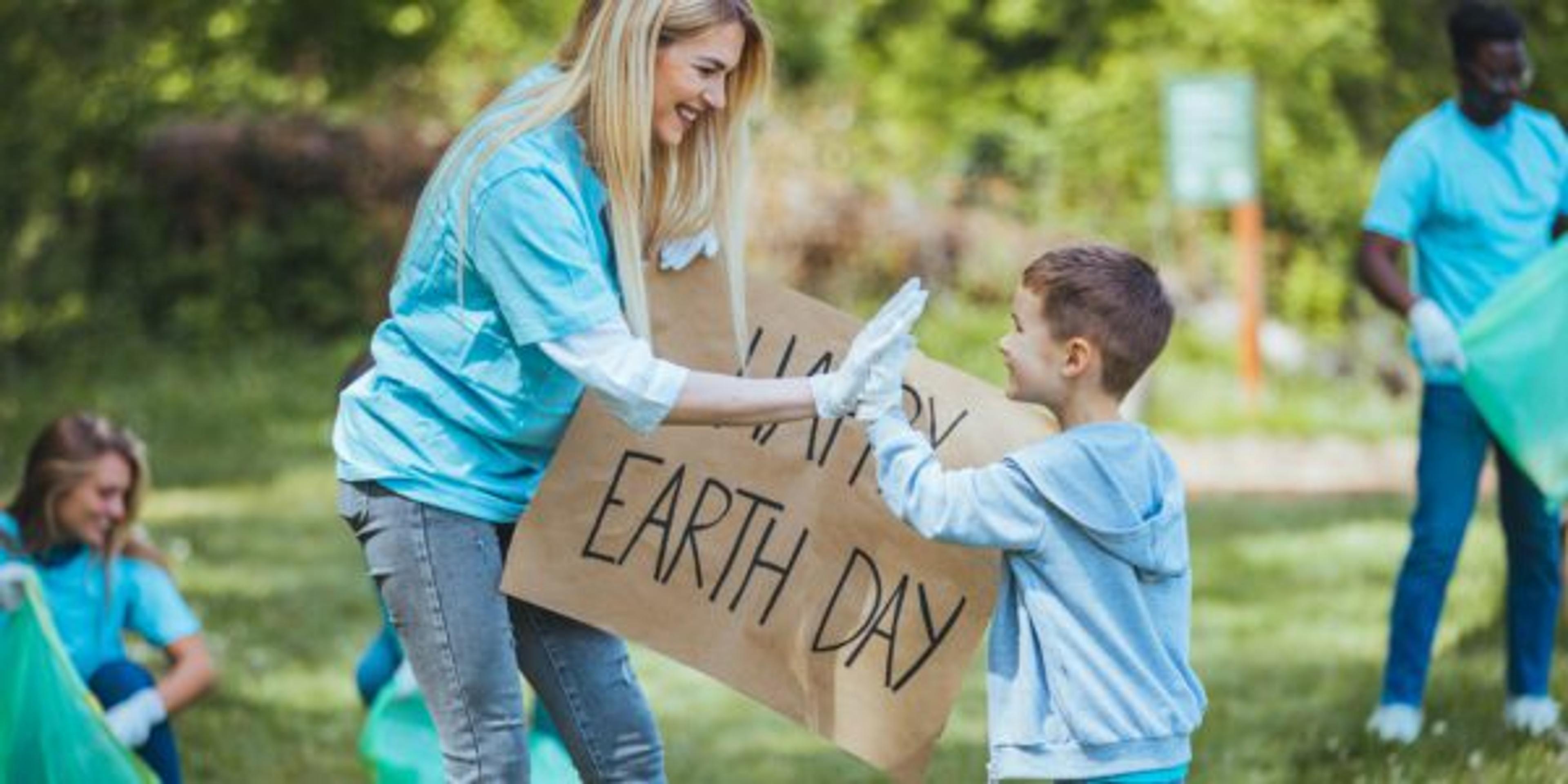 Vvolunteering, charity, cleaning, people and ecology concept - Mother and son volunteers with garbage bags cleaning area in park. Young volunteers cleaning up the forest together