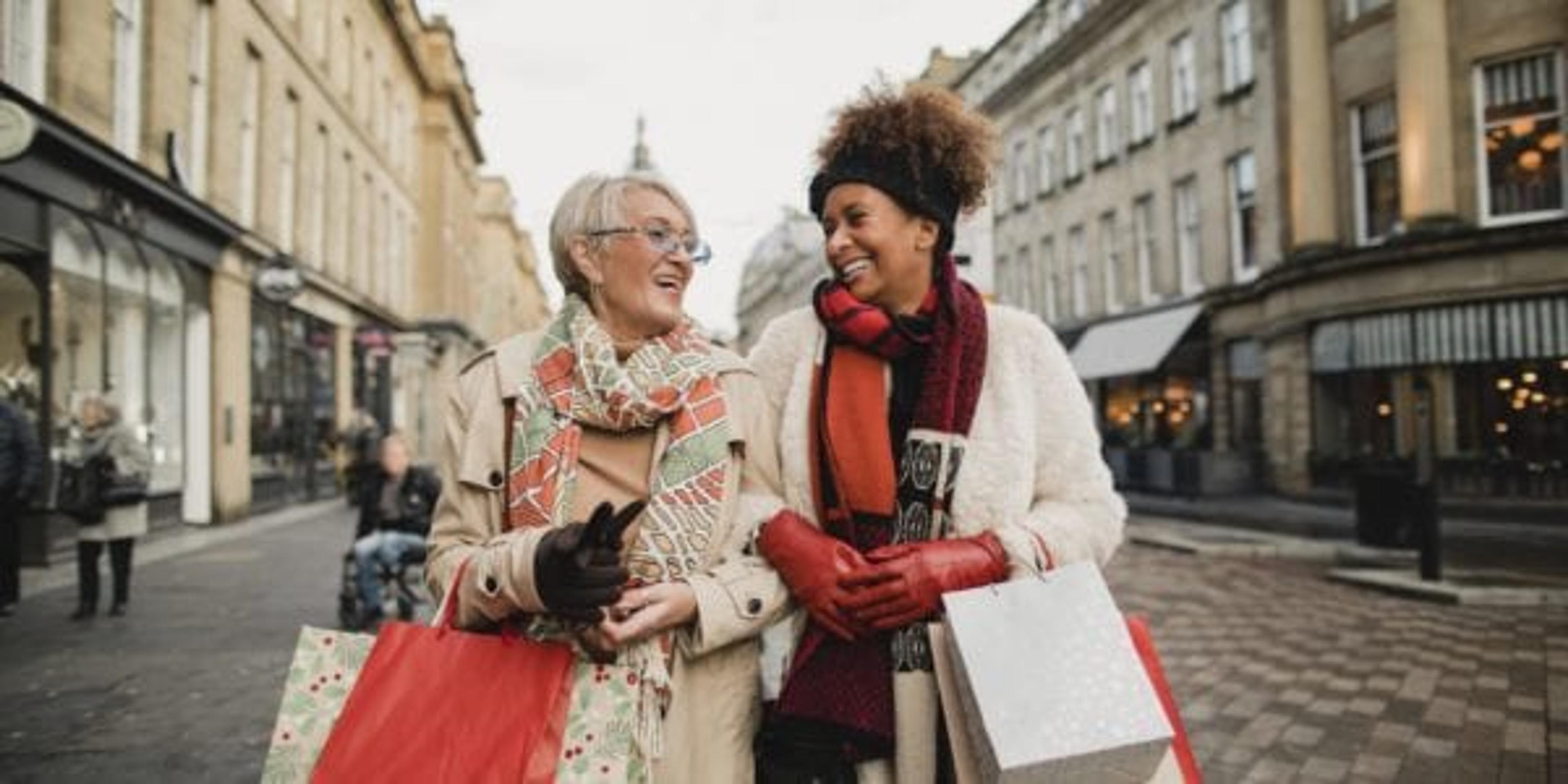 Two women walk down a city street holding shopping bags