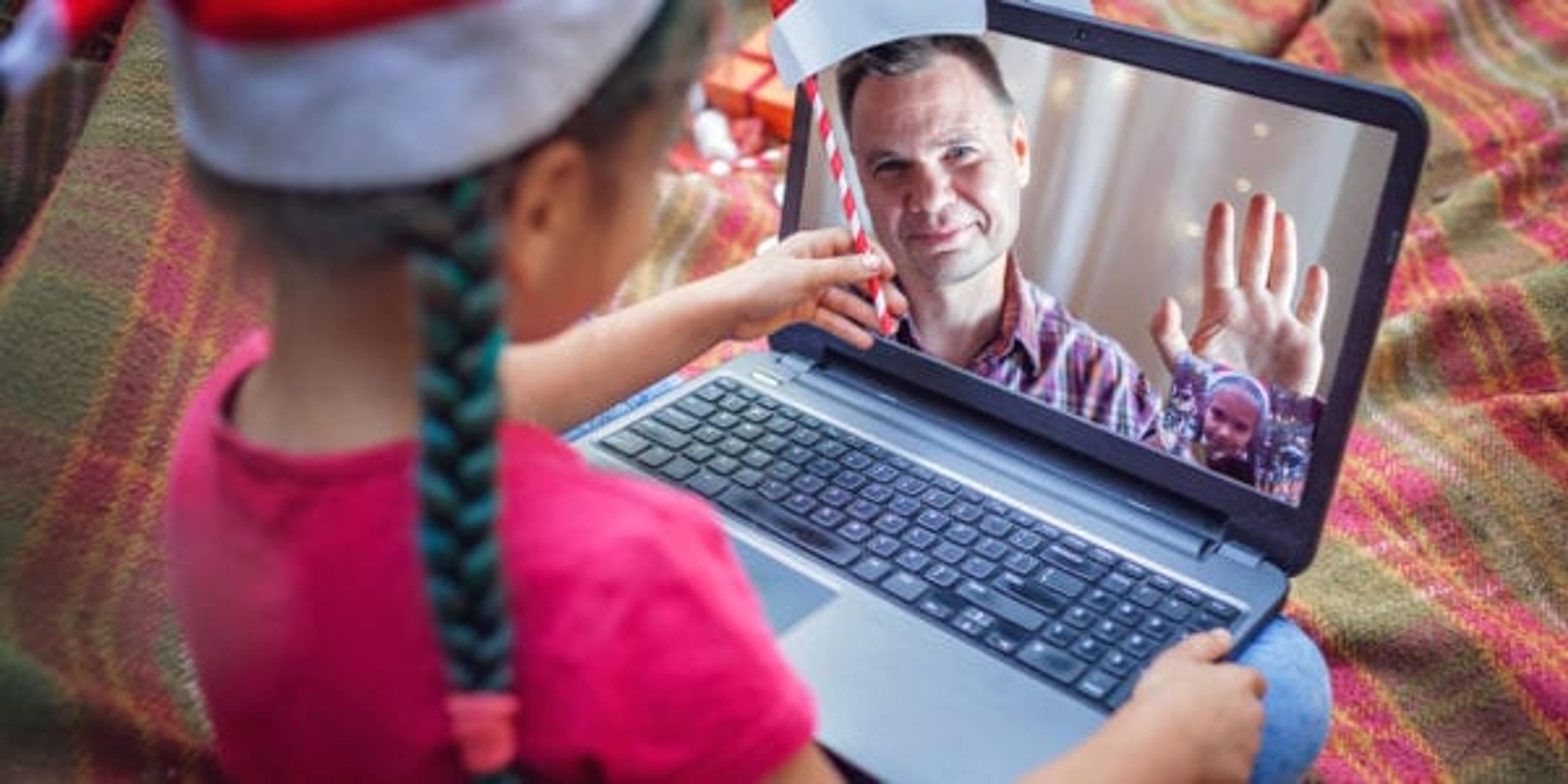 New normal online Christmas celebration. Cute sibling using laptop and festive fun props to celebrate Christmas with father via video chat, happy holidays, outdoor