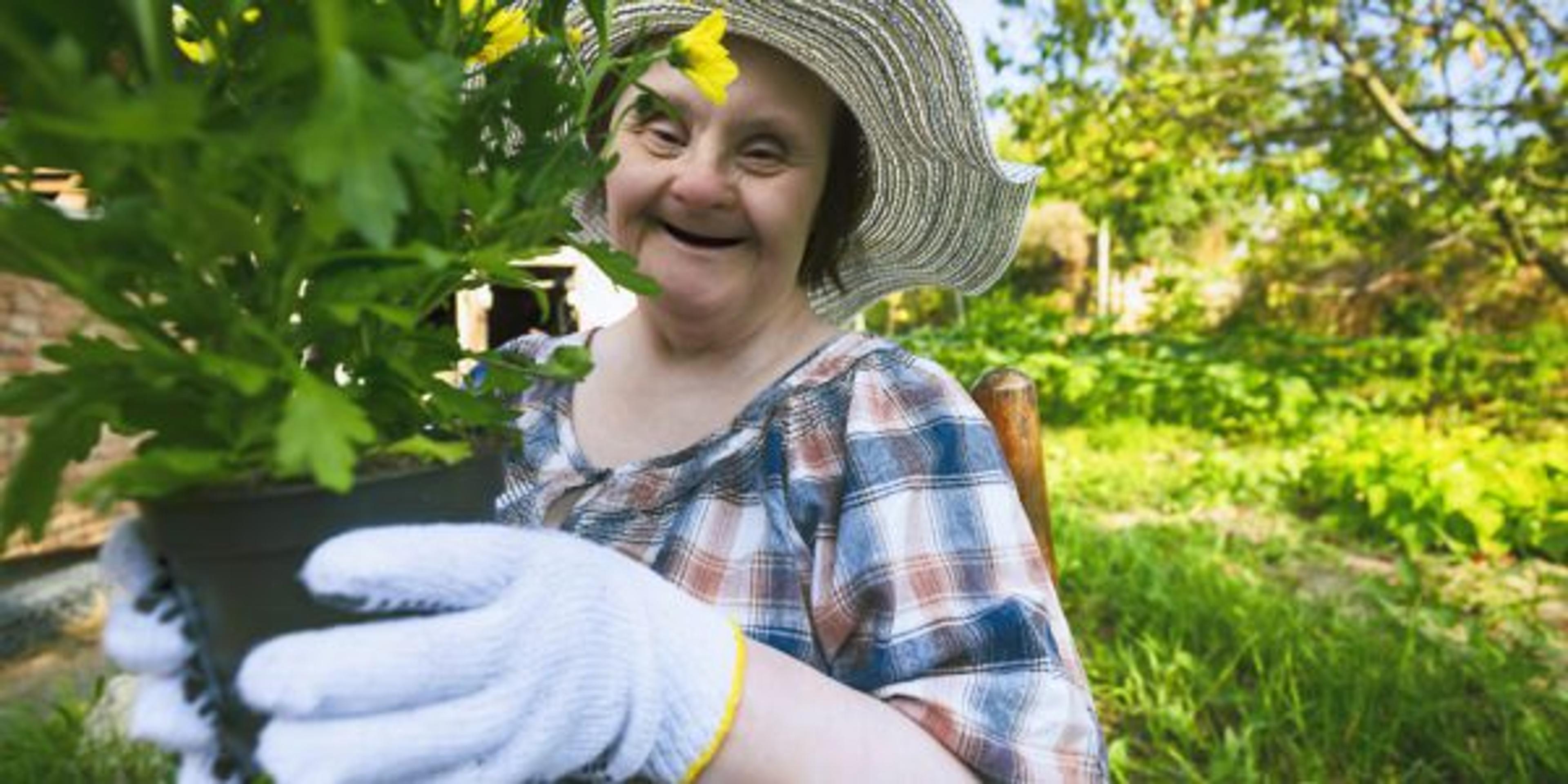 Happy woman with Down Syndrome ready to planting flowers. Gardening.