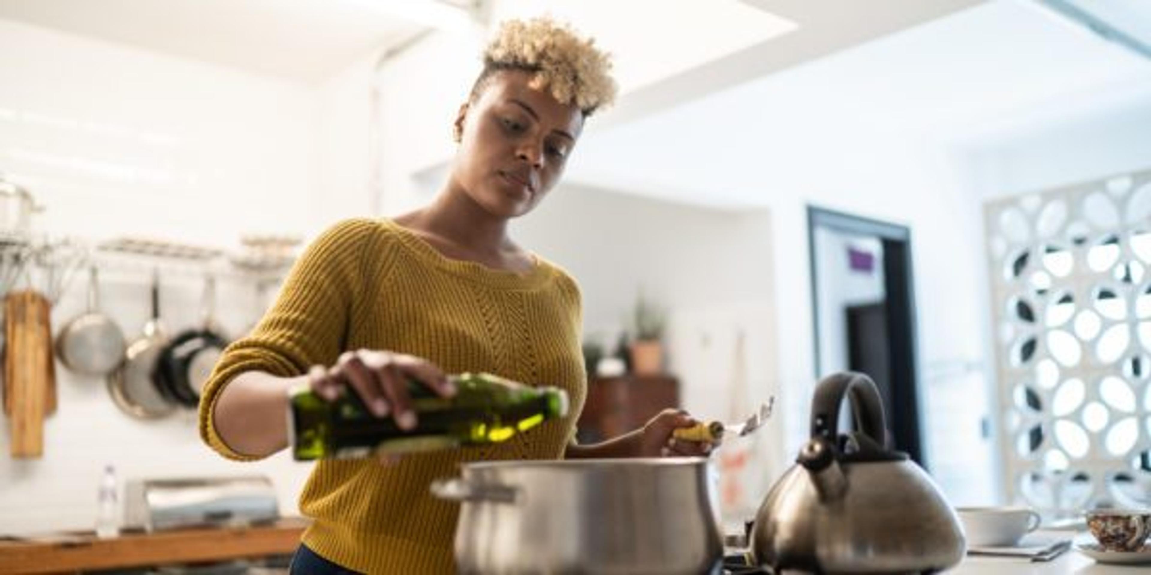 Young woman preparing food at home using olive oil