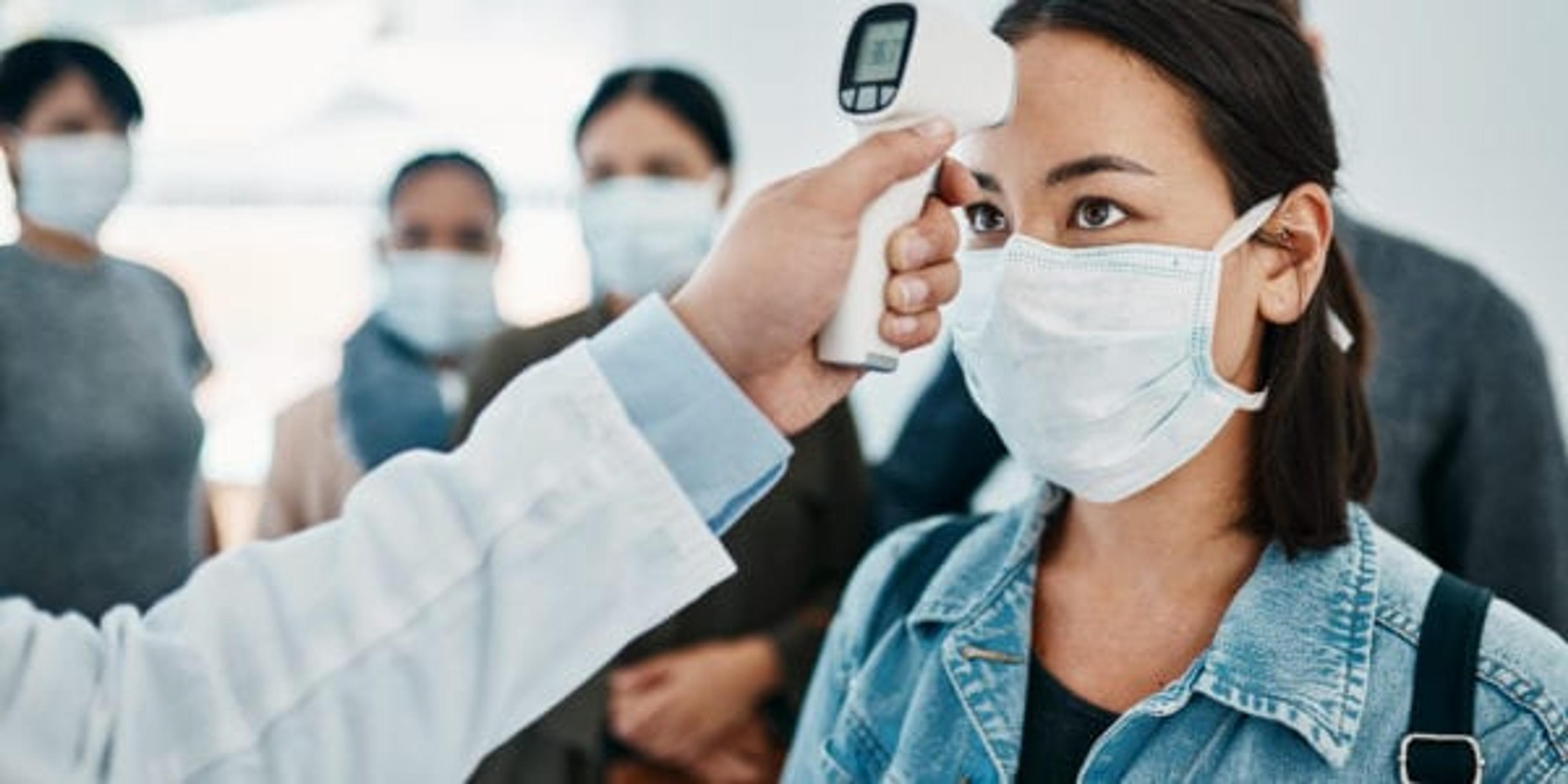 Shot of a young woman getting her temperature taken with an infrared thermometer by a doctor during an outbreak