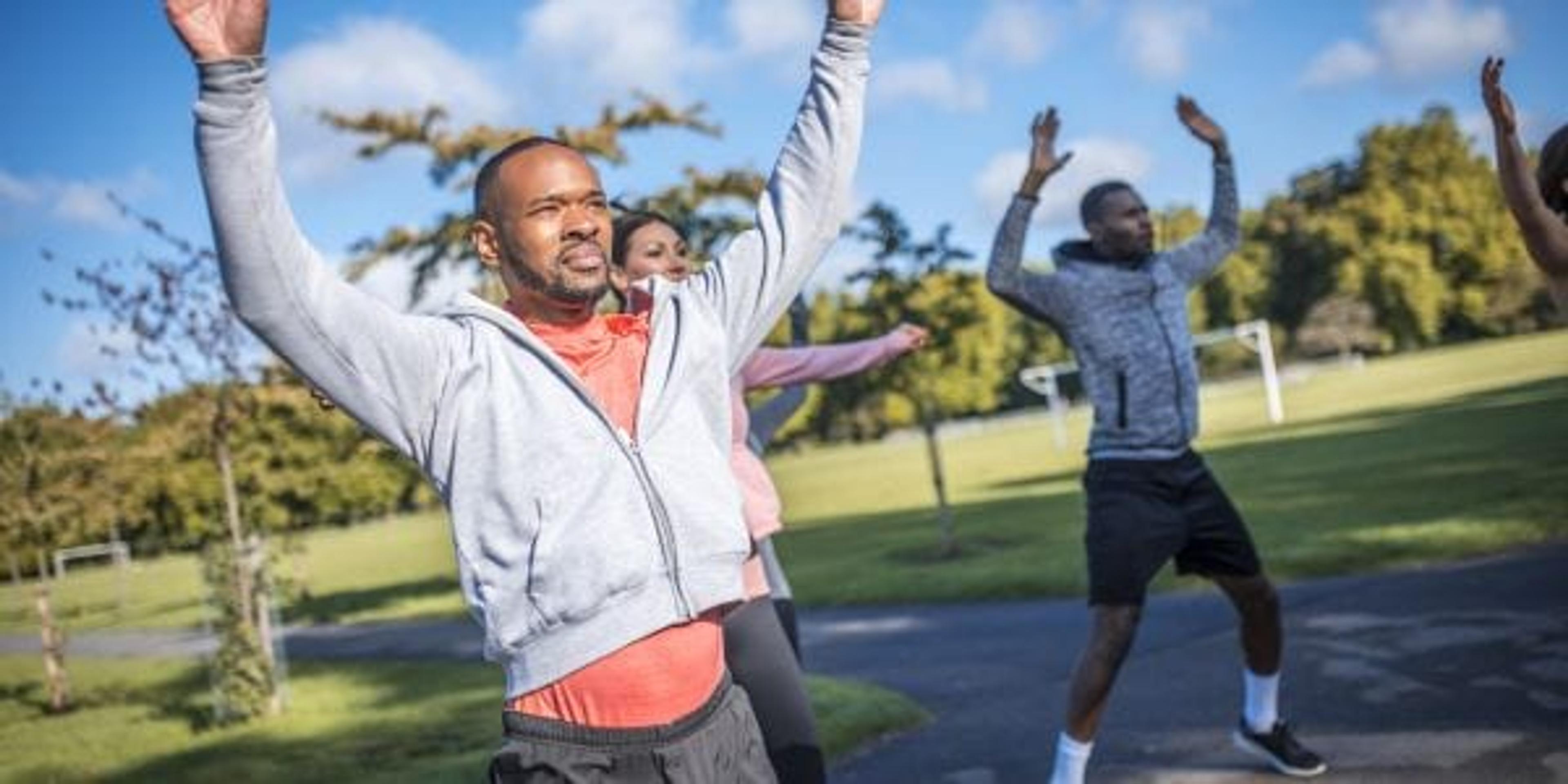 Group of friends exercising outdoors in a park on a sunny day. They are doing jumping jacks.