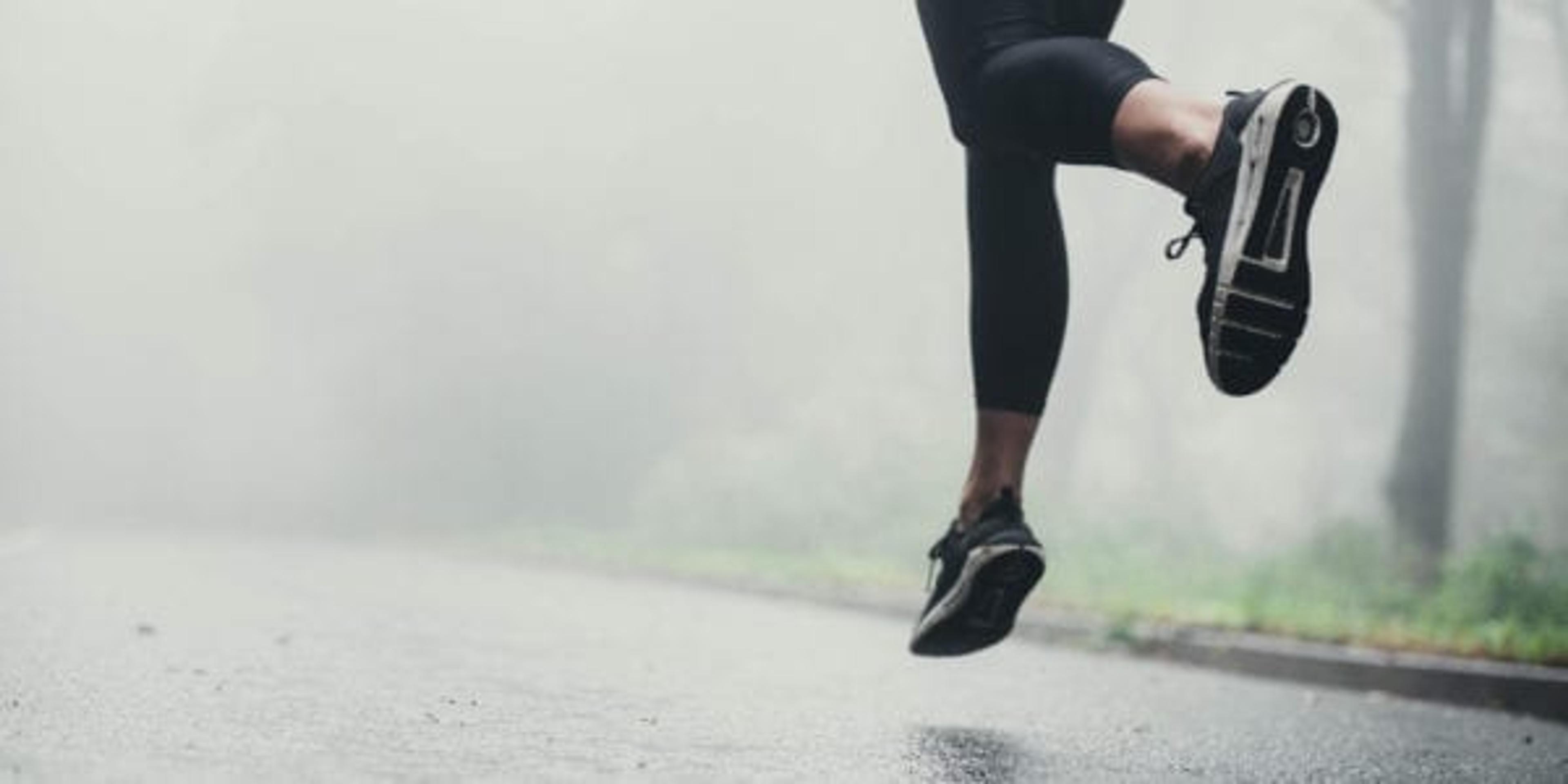 Unrecognizable athletic woman running on the road during foggy day in nature.