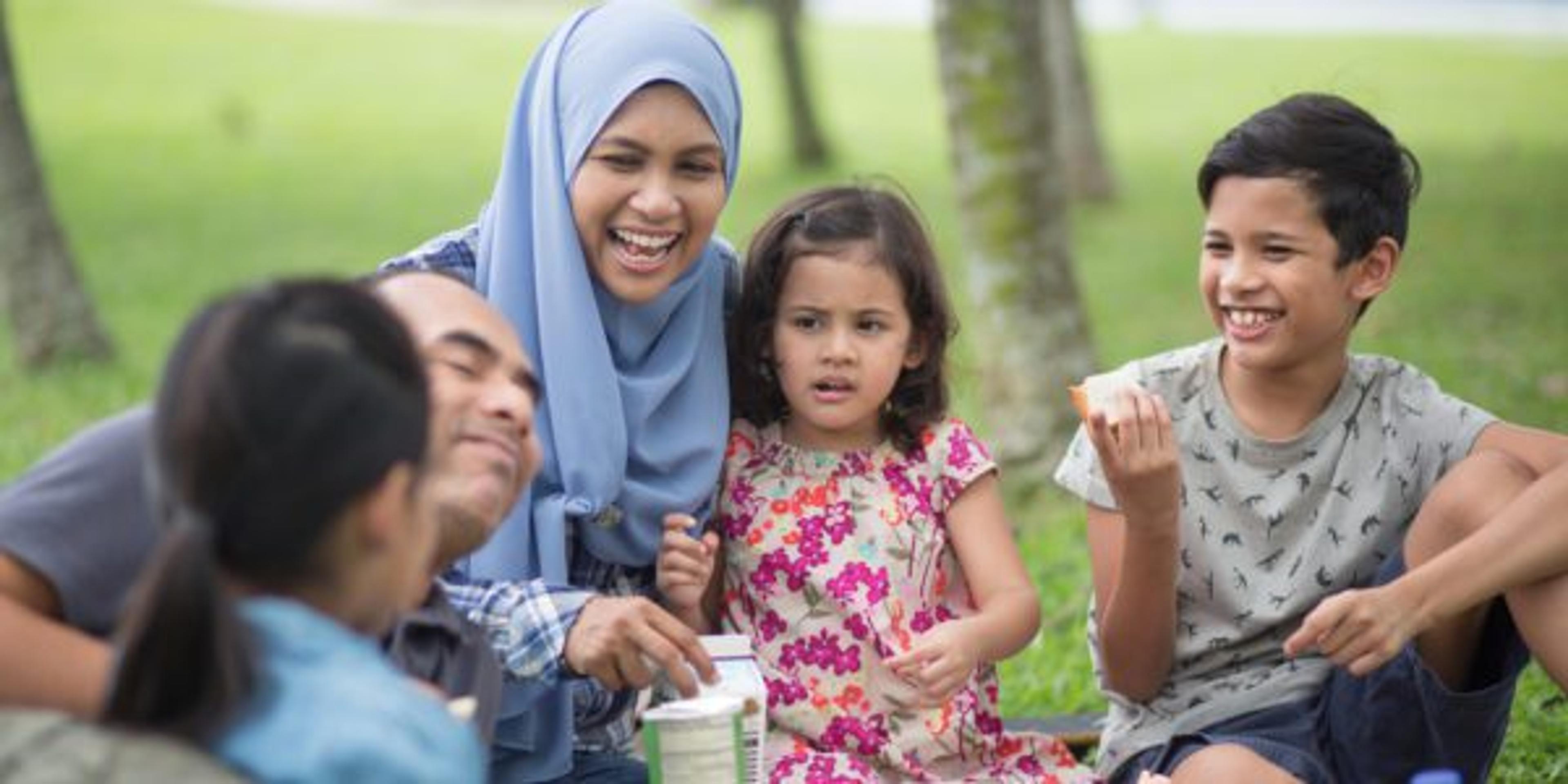 Happy family enjoying food in picnic. Laughing woman and children looking at man in park. They are spending leisure time together on weekend.