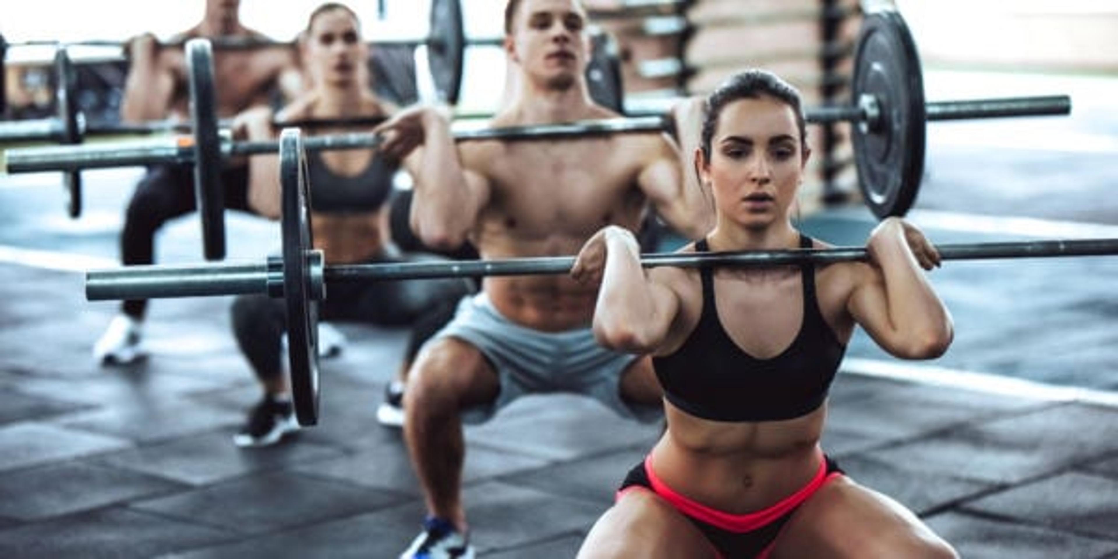 Group of people training in a gym squatting with barbells