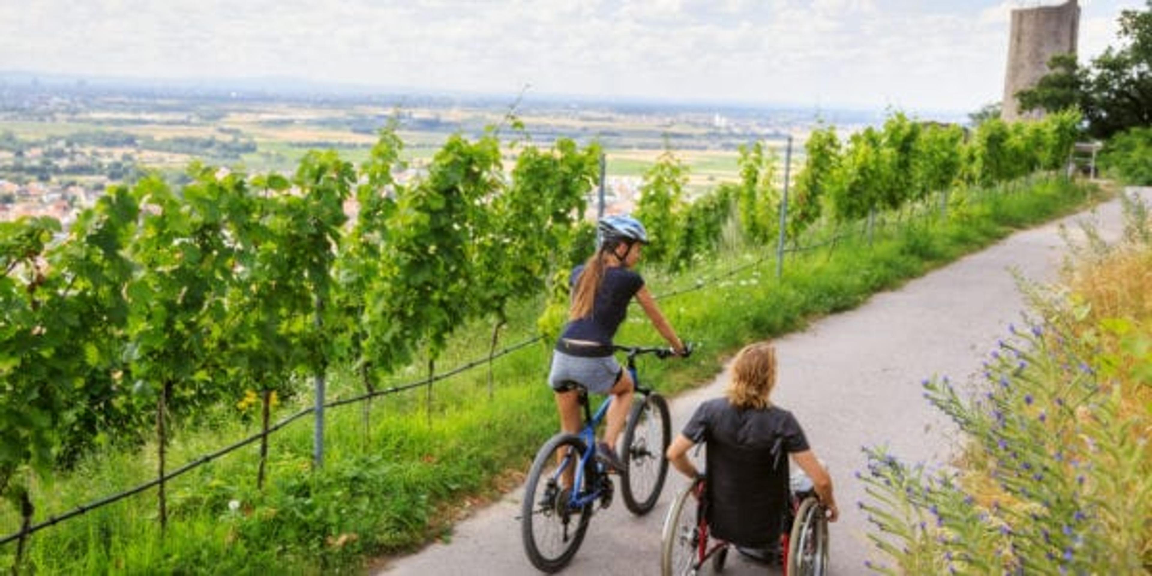 Young couple enjoying time outdoors. She is cycling, he is sitting in a wheelchair.