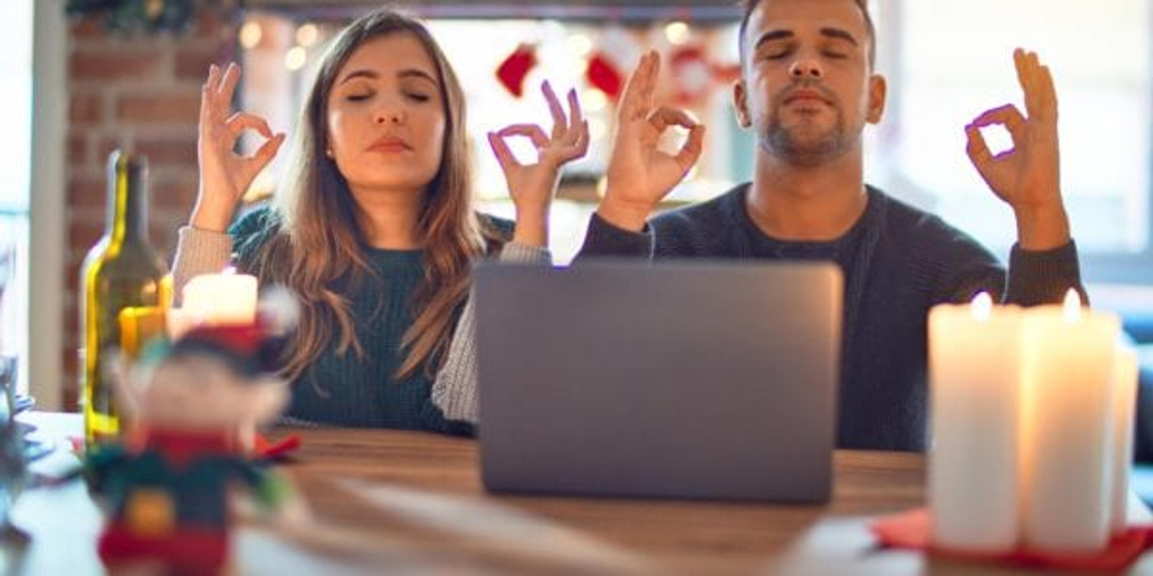 Young beautiful couple sitting using laptop around christmas decoration at home relax and smiling with eyes closed doing meditation gesture with fingers. Yoga concept.