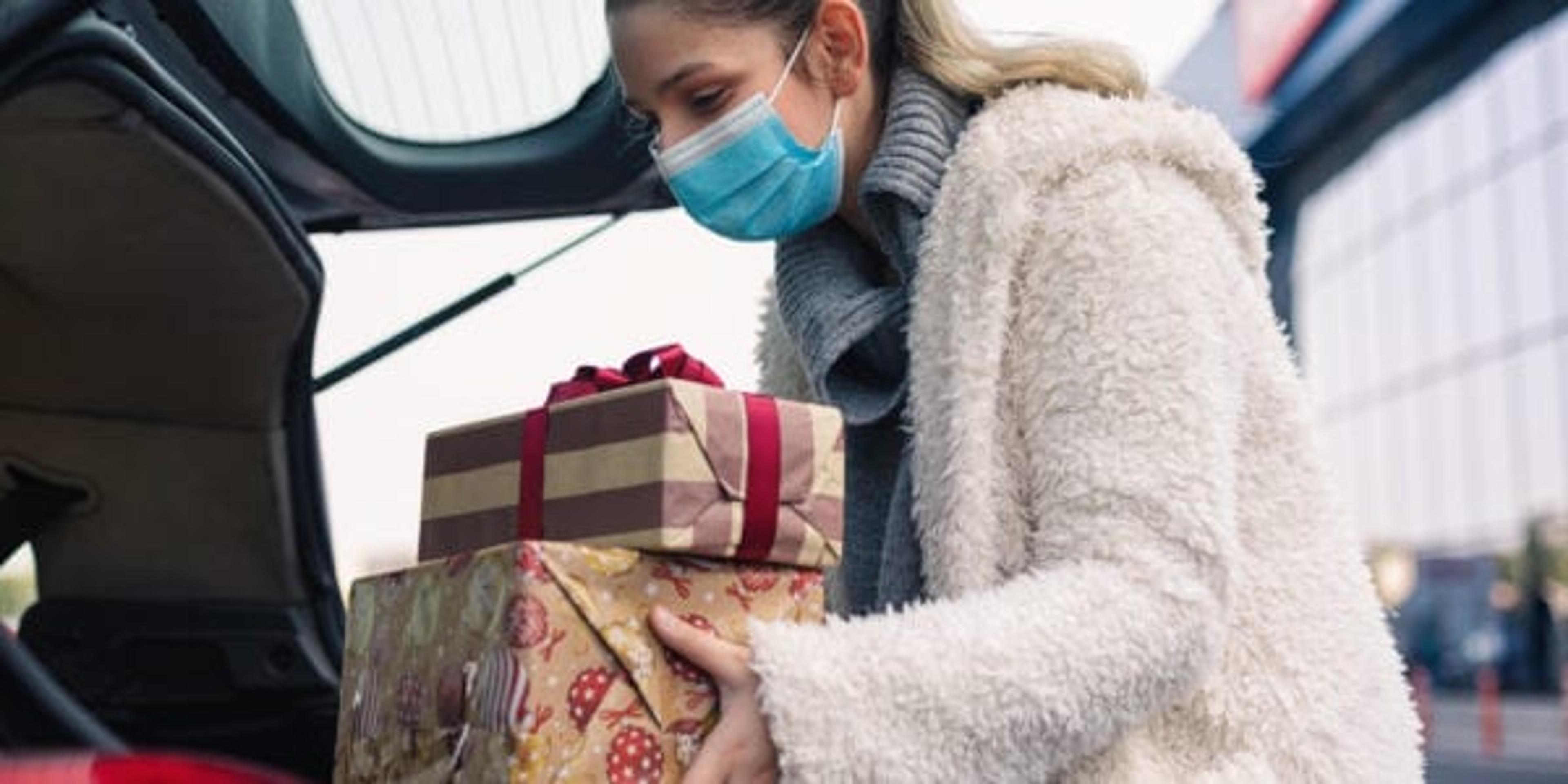 Teenage girl packing Christmas gifts in a car after shopping. She wears a protective mask to protect from corona virus COVID-19.