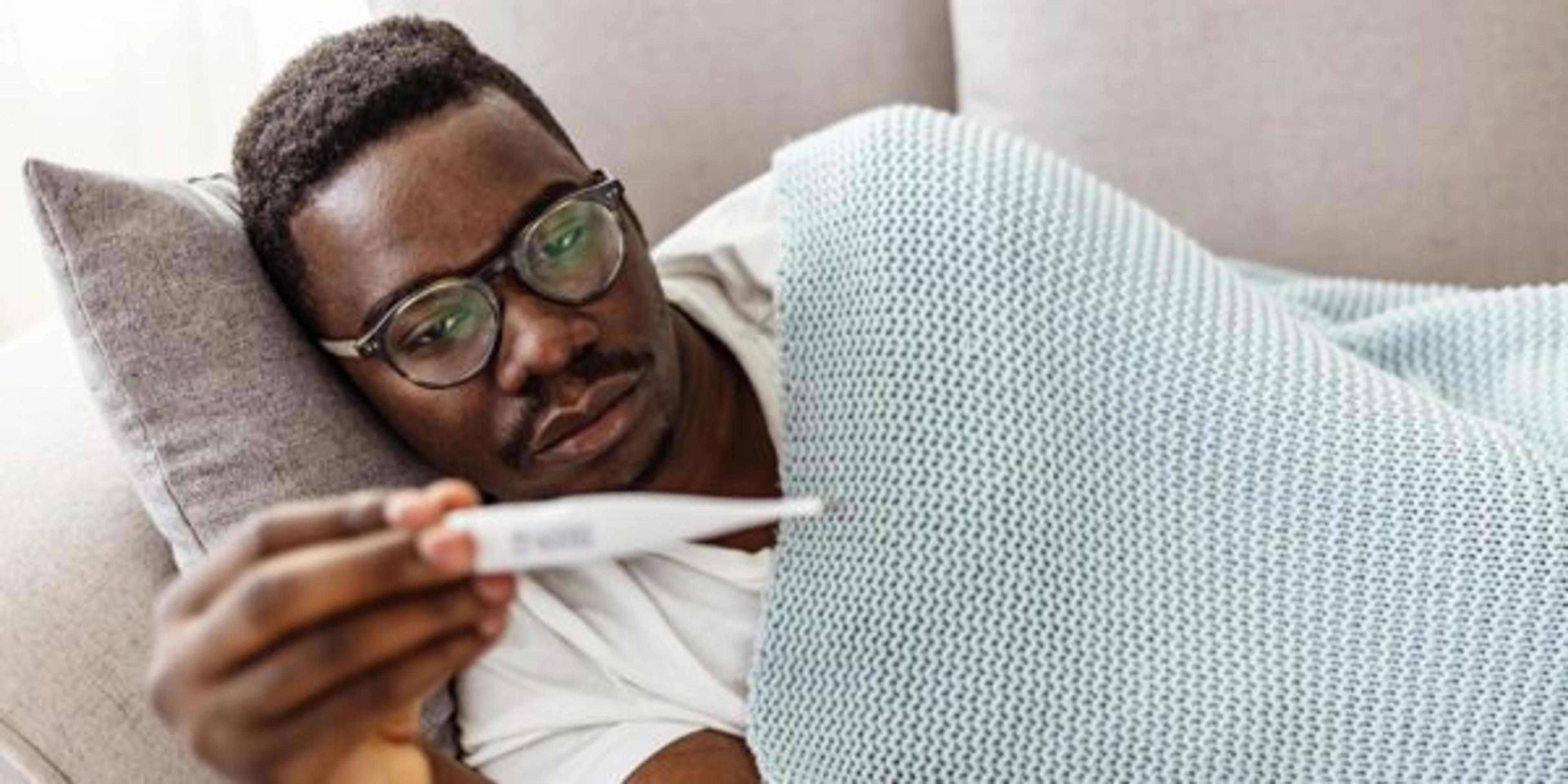 Man lying on the couch with a high fever checks a thermometer