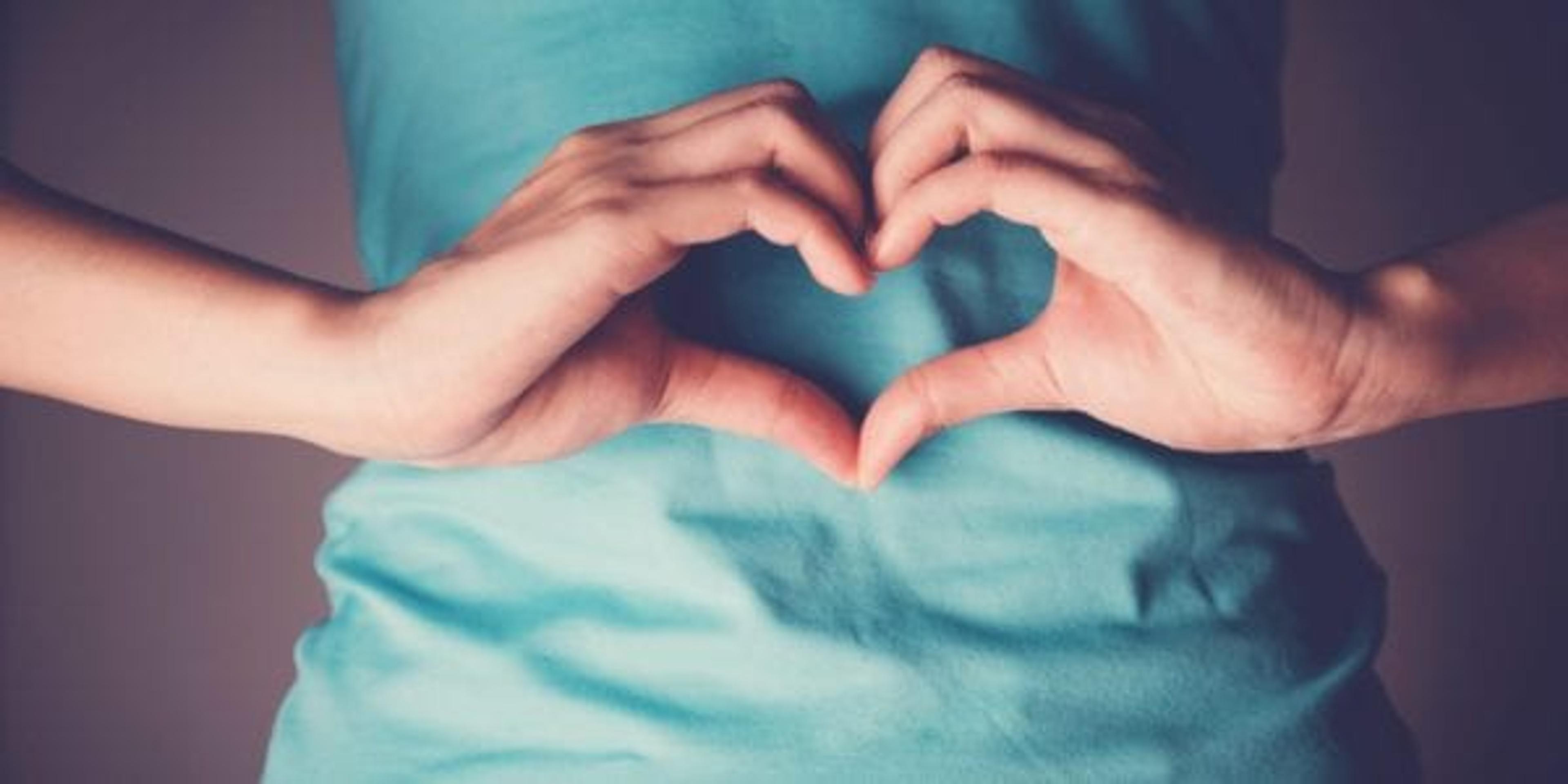 Woman's hands making a heart shape on her stomach.