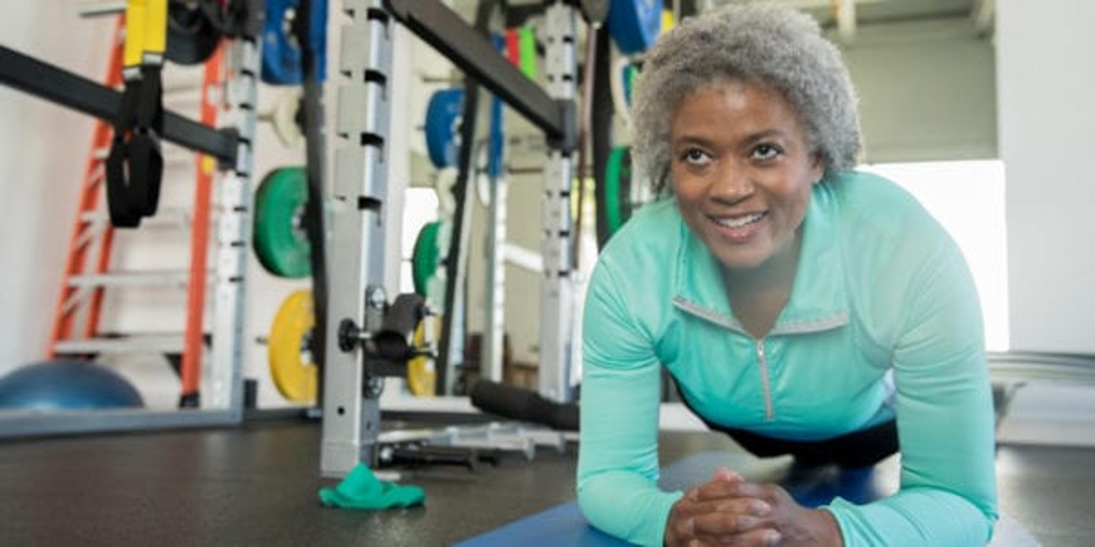 Senior woman smiling while doing a planking exercise in modern gym