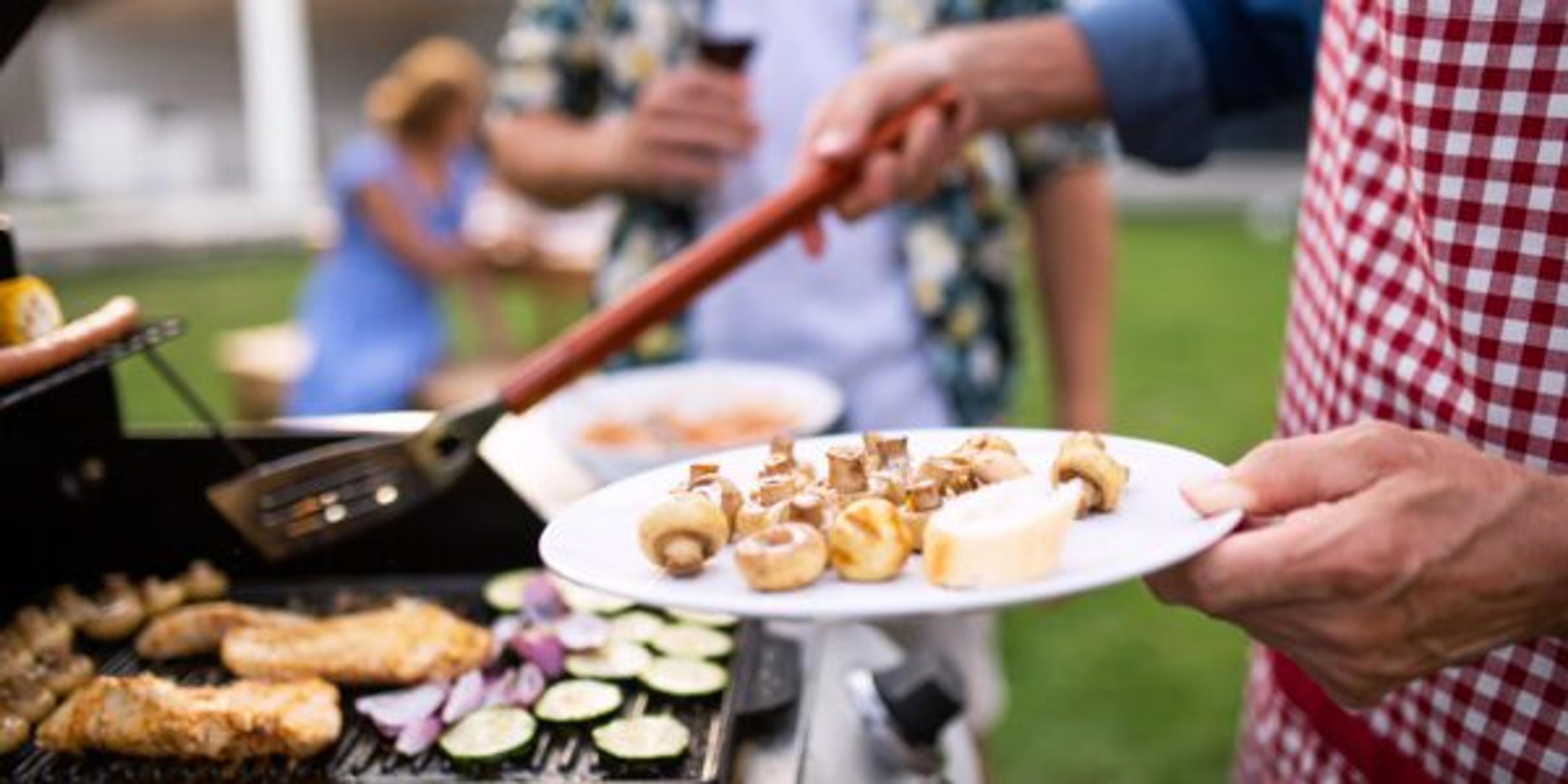 Midsection of family outdoors on garden barbecue, grilling.