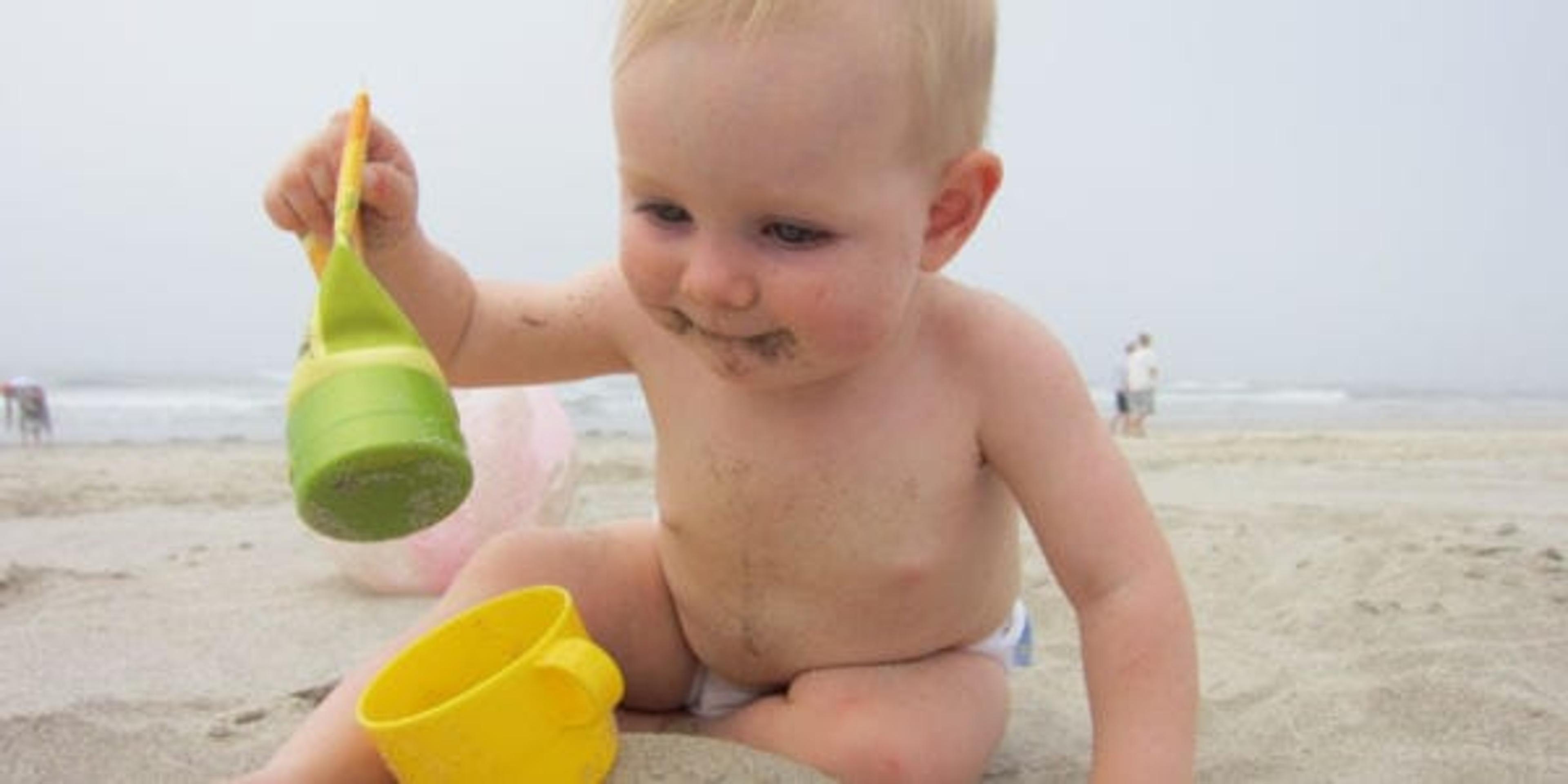 Image of a baby playing on the beach with sand toys.