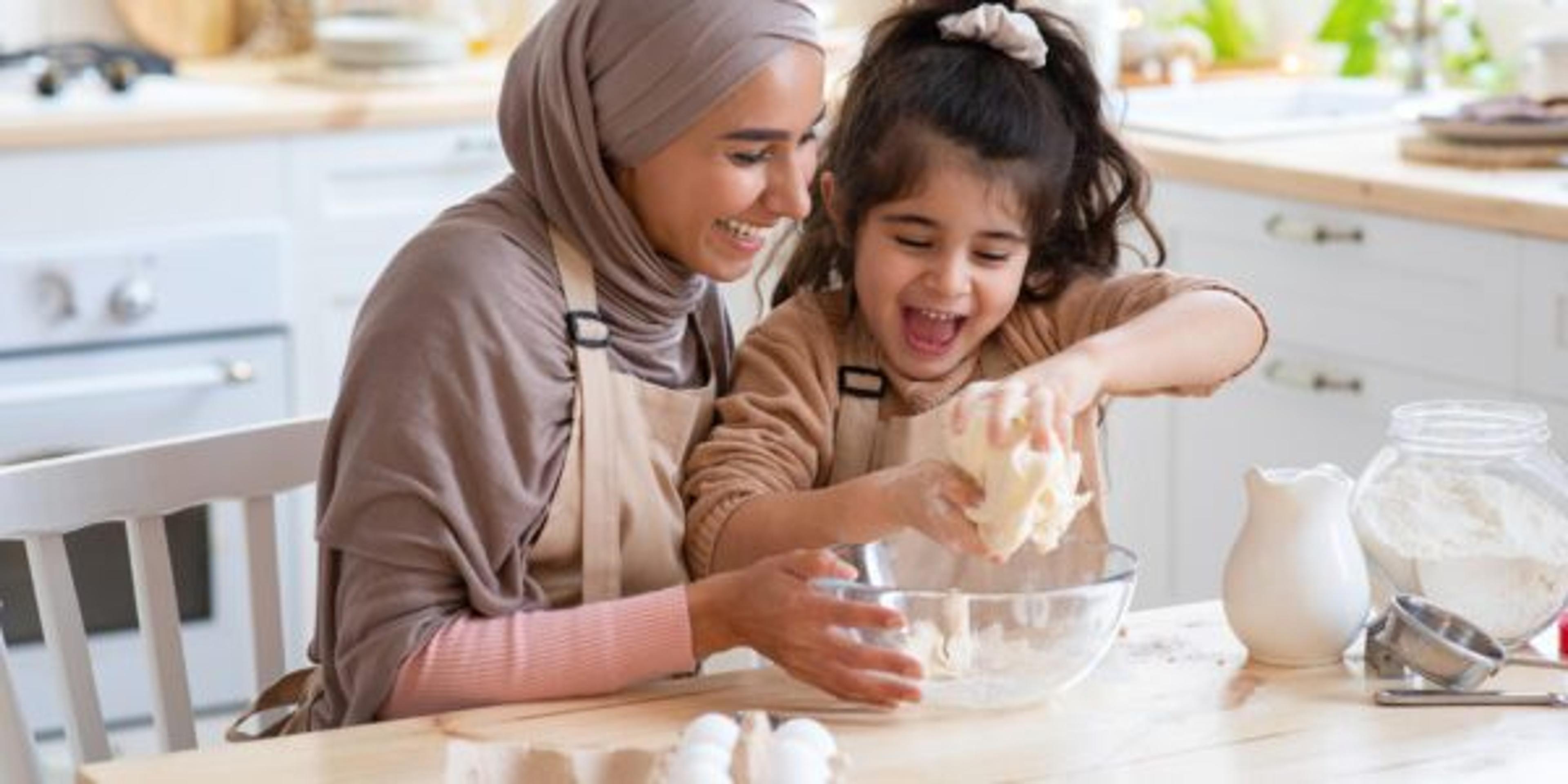 A Muslim mom and daughter have fun baking together in their kitchen.