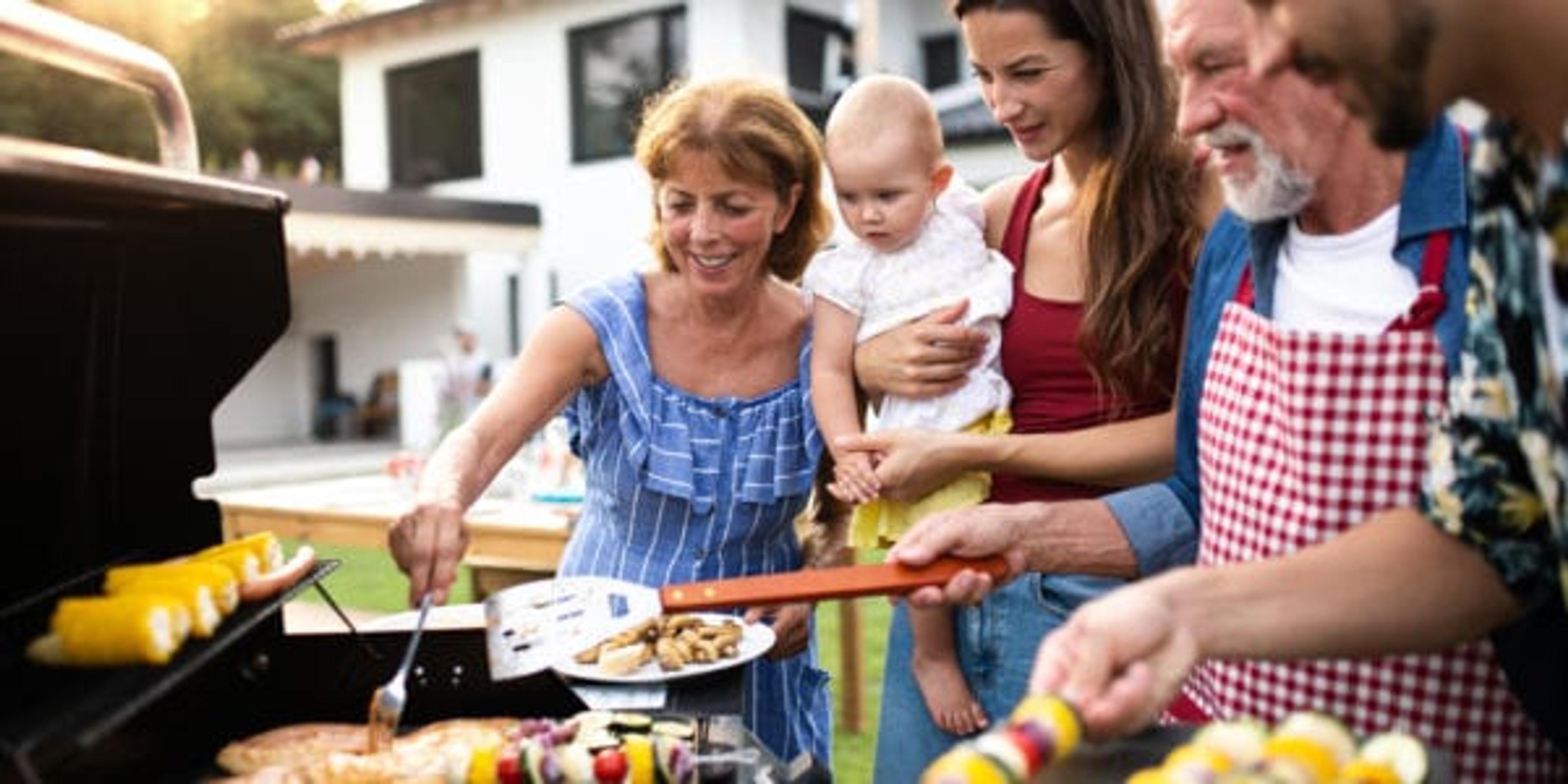 Portrait of multigeneration family outdoors on garden barbecue, grilling and talking.