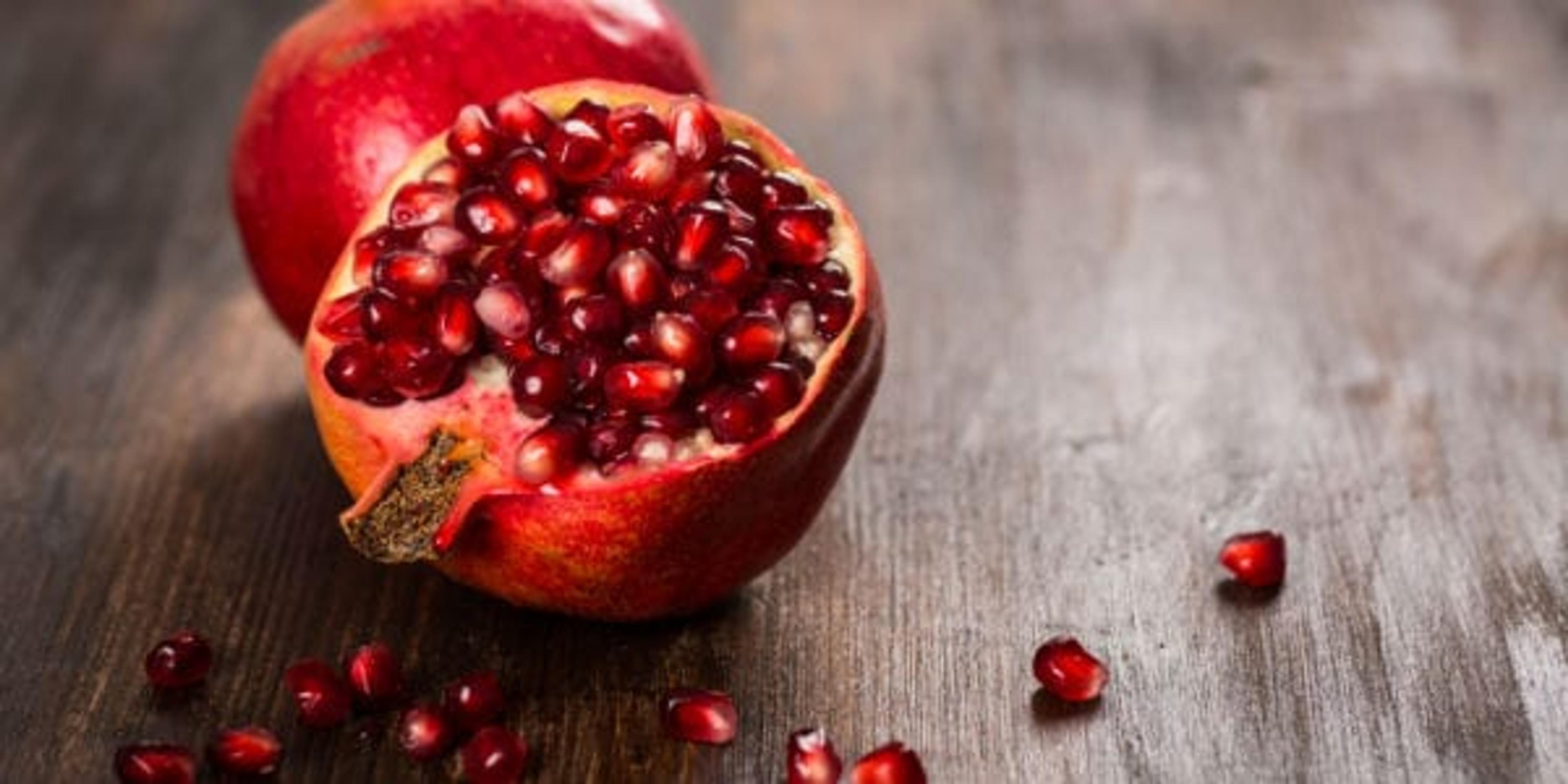 Open pomegranate wtih seeds spilling on table.