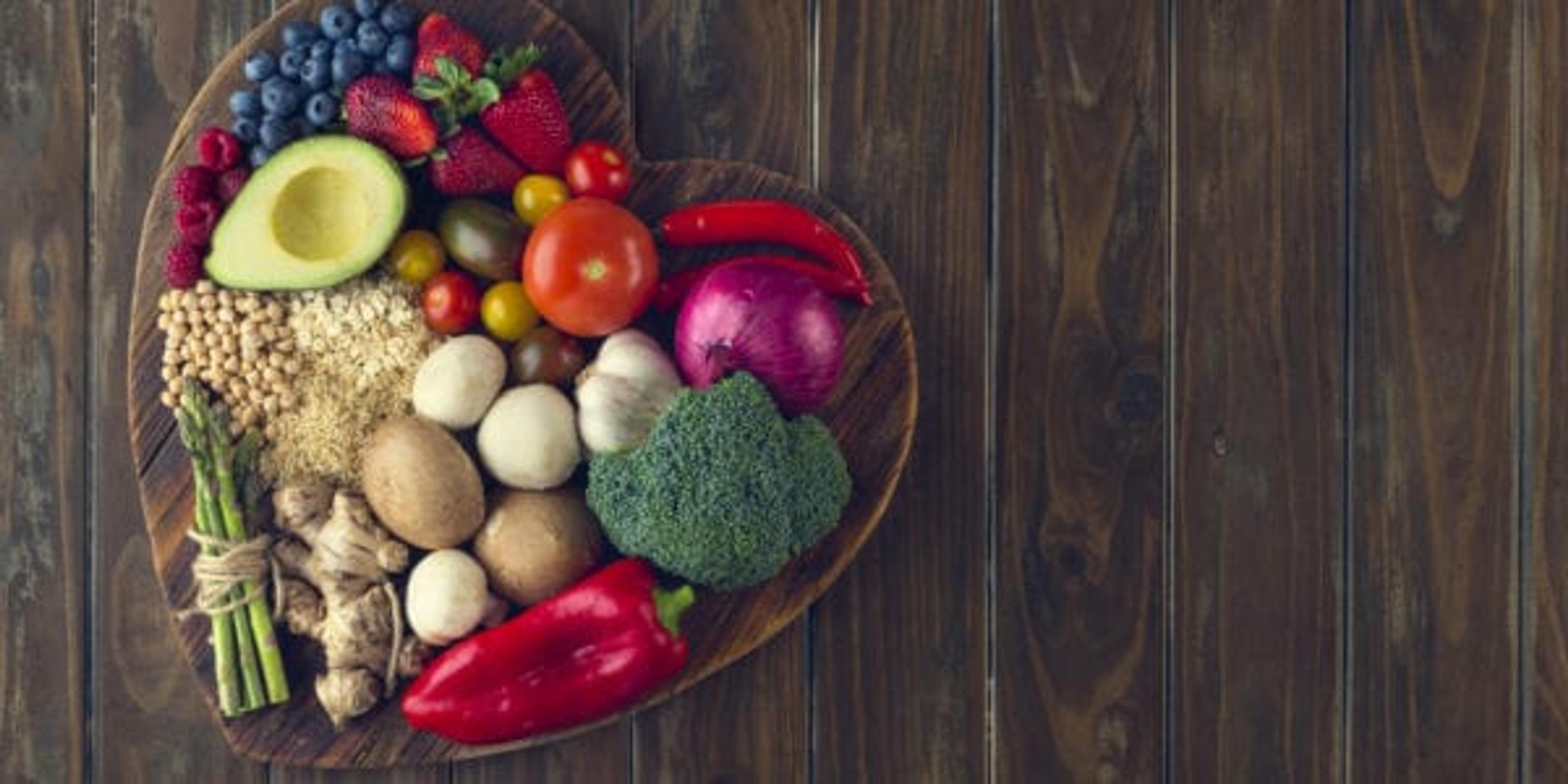 Healthy food on a heart shape cutting board. Love of food concept with fruit, vegetables, grains and high fibre foods. Rustic wood textures