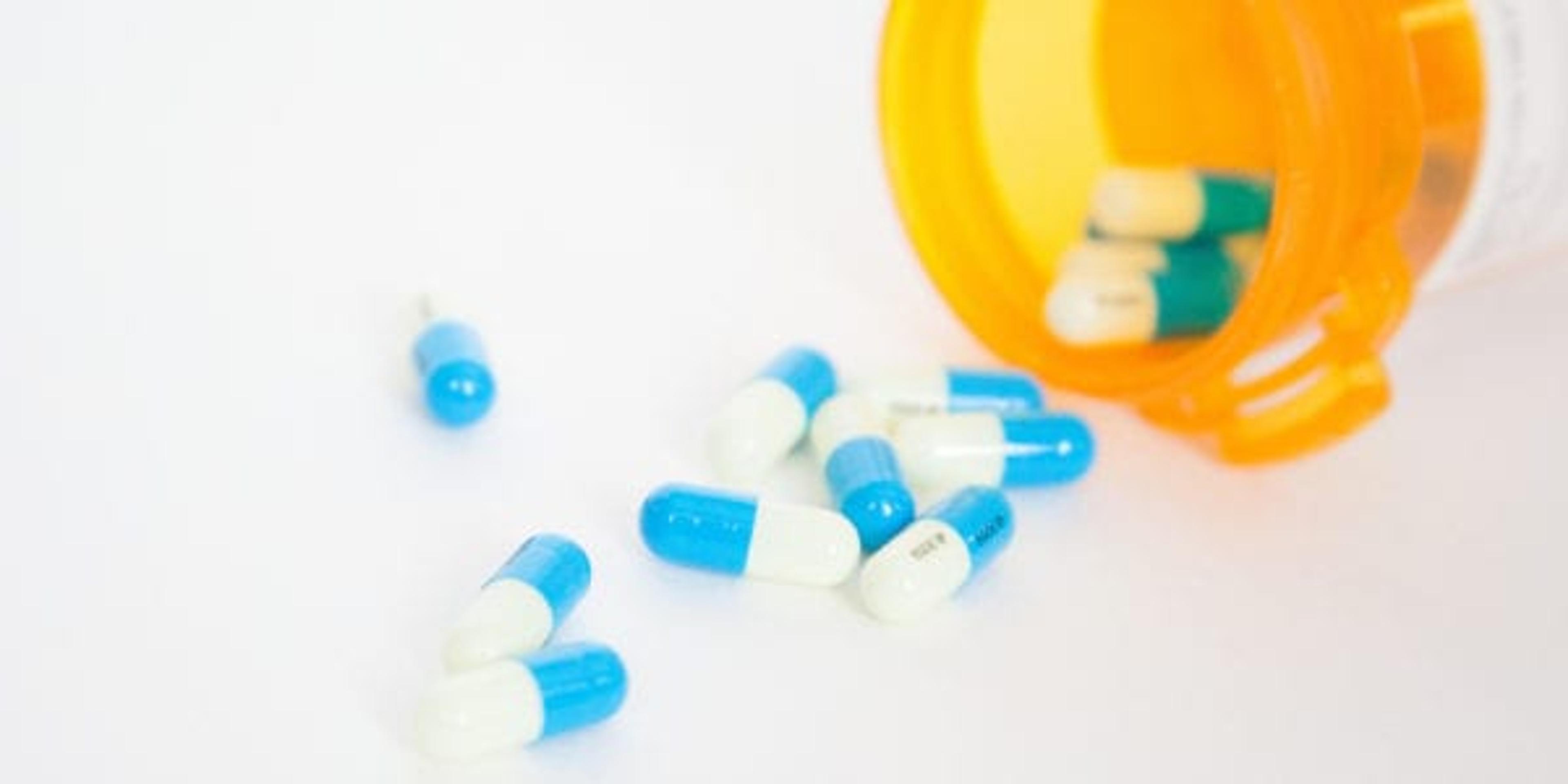 bottle of blue and white pills spilling out of a prescription bottle