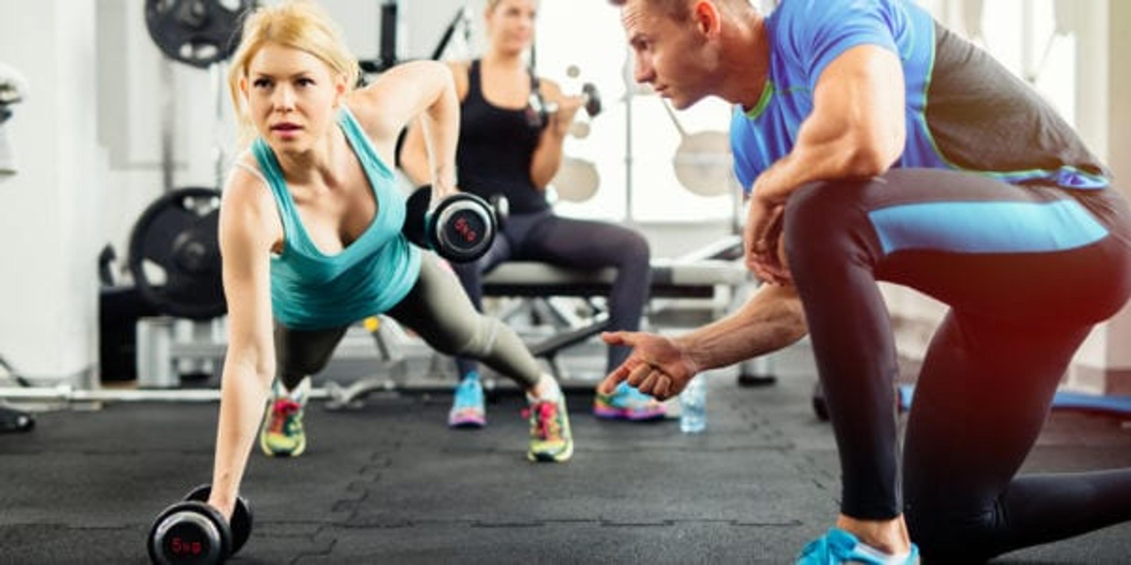 Sporty woman doing push-ups under supervision of personal trainer.