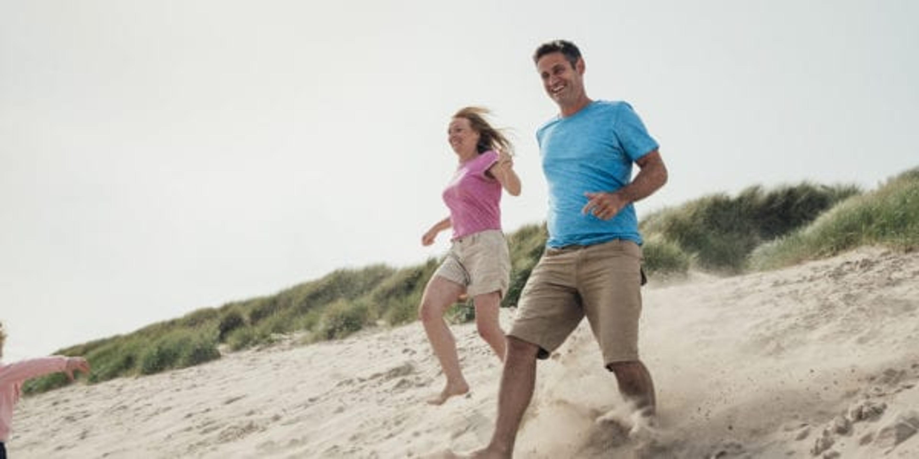 Low angle view of couple racing down a sand dune while on holiday at the seaside.
