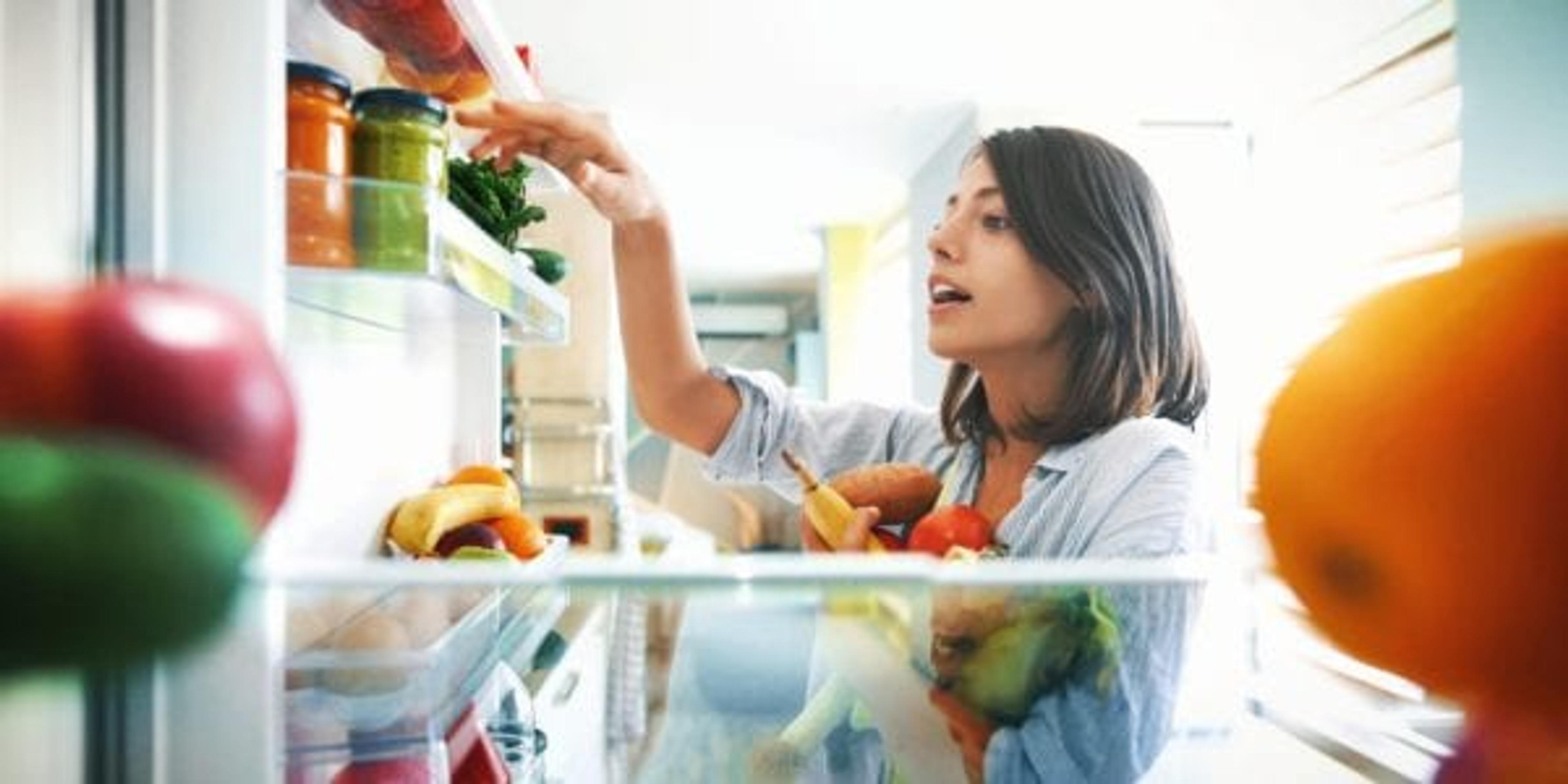 Closeup of a cheerful young couple picking some fruit and veggies from the fridge to make some healthy breakfast on Sunday morning. Shot from inside the working fridge.