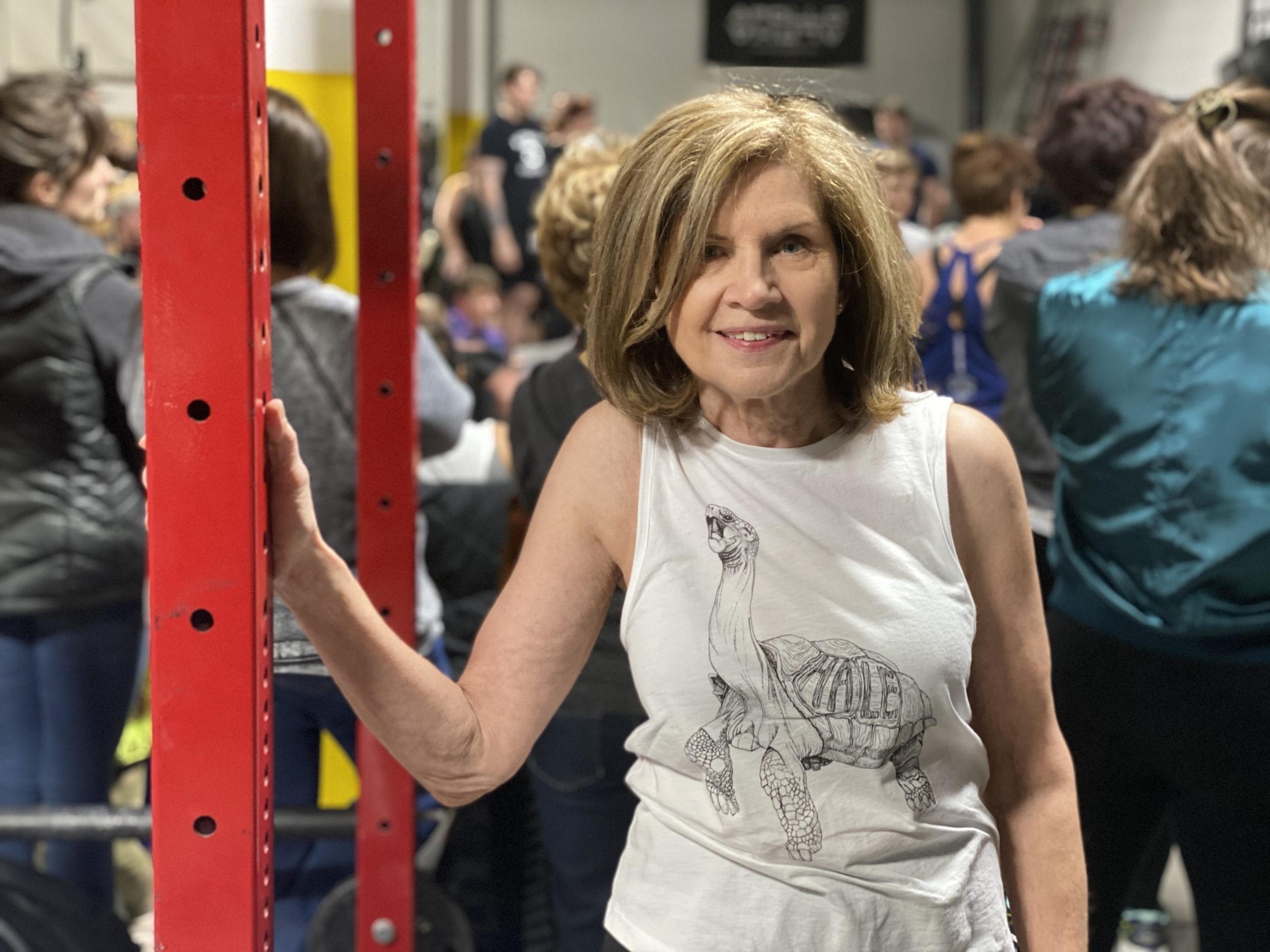 A senior woman poses for a photo in a weightlifting gym