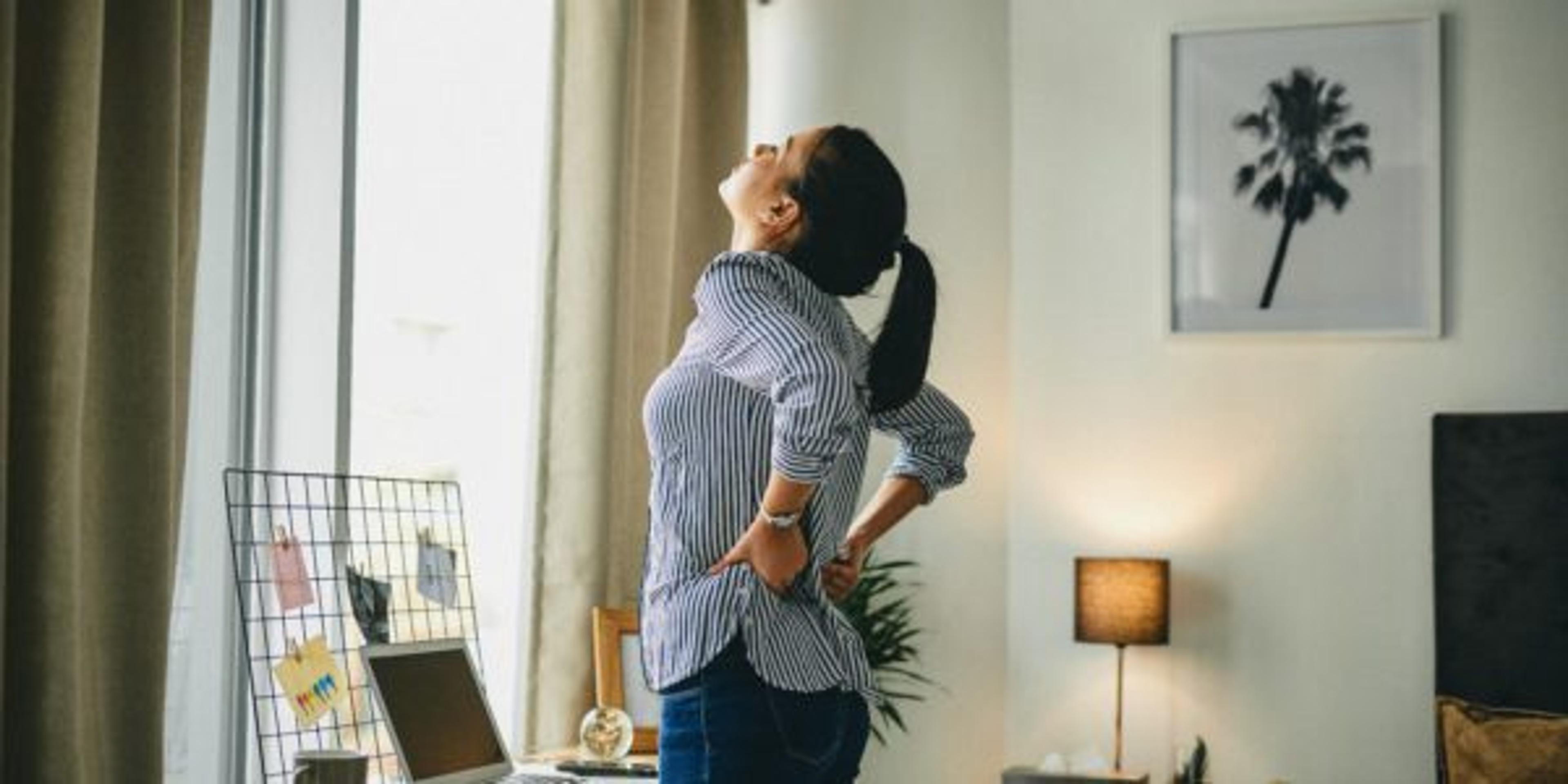 Rearview shot of a young woman suffering with back pain while working from home