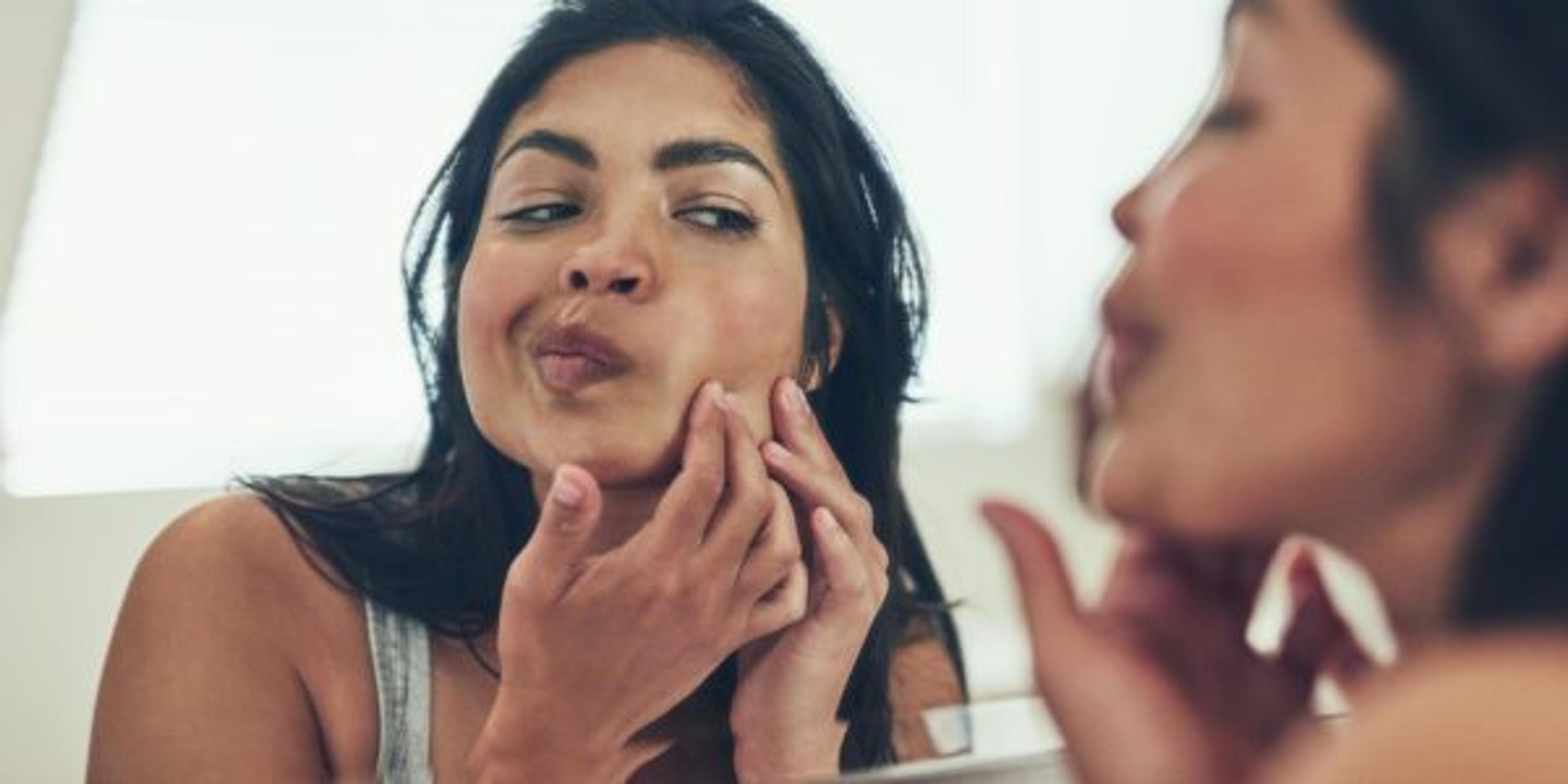 Shot of a young woman squeezing a pimple on her face at home