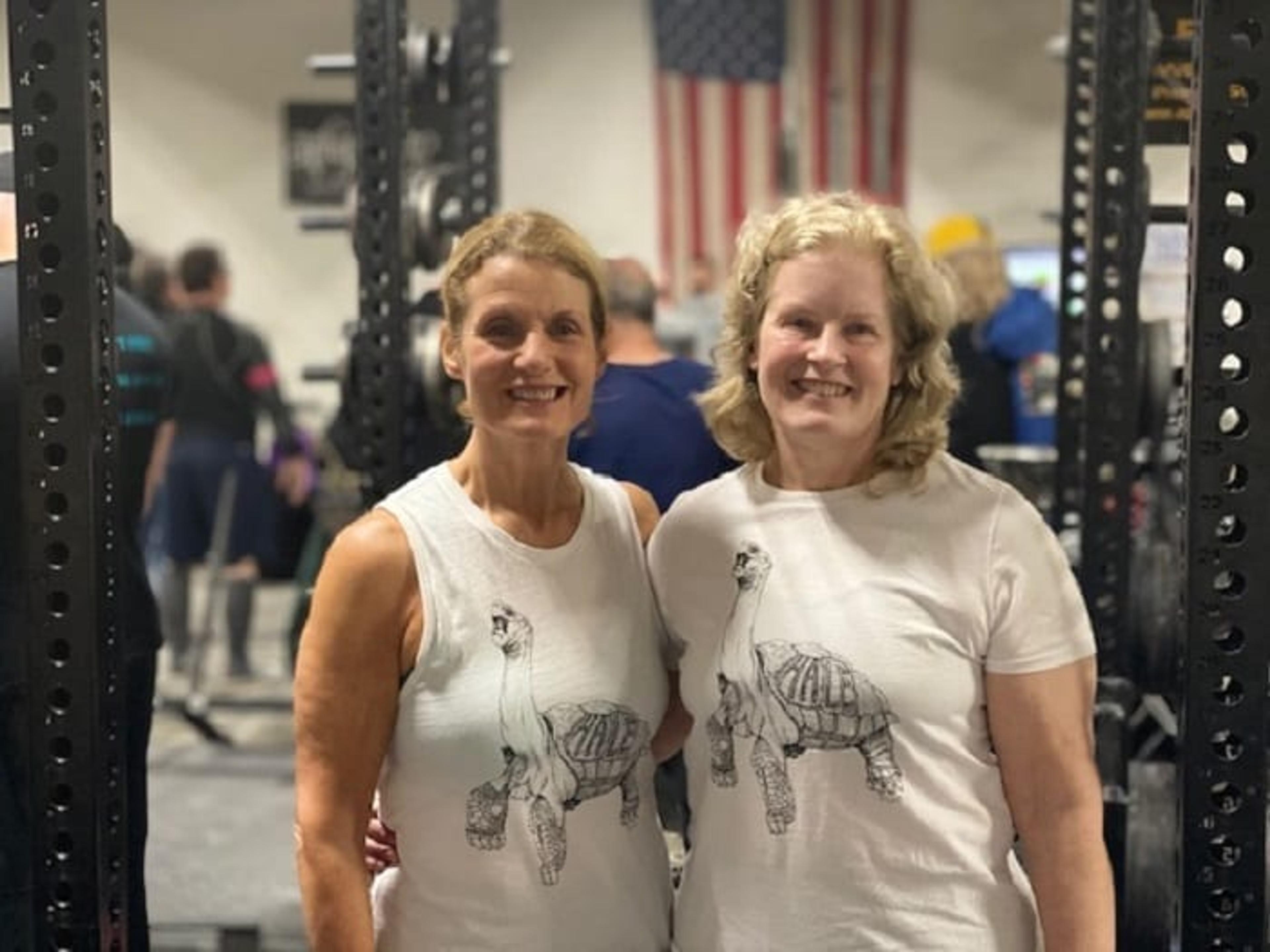 Two 60+ women pose for a photo in a gym