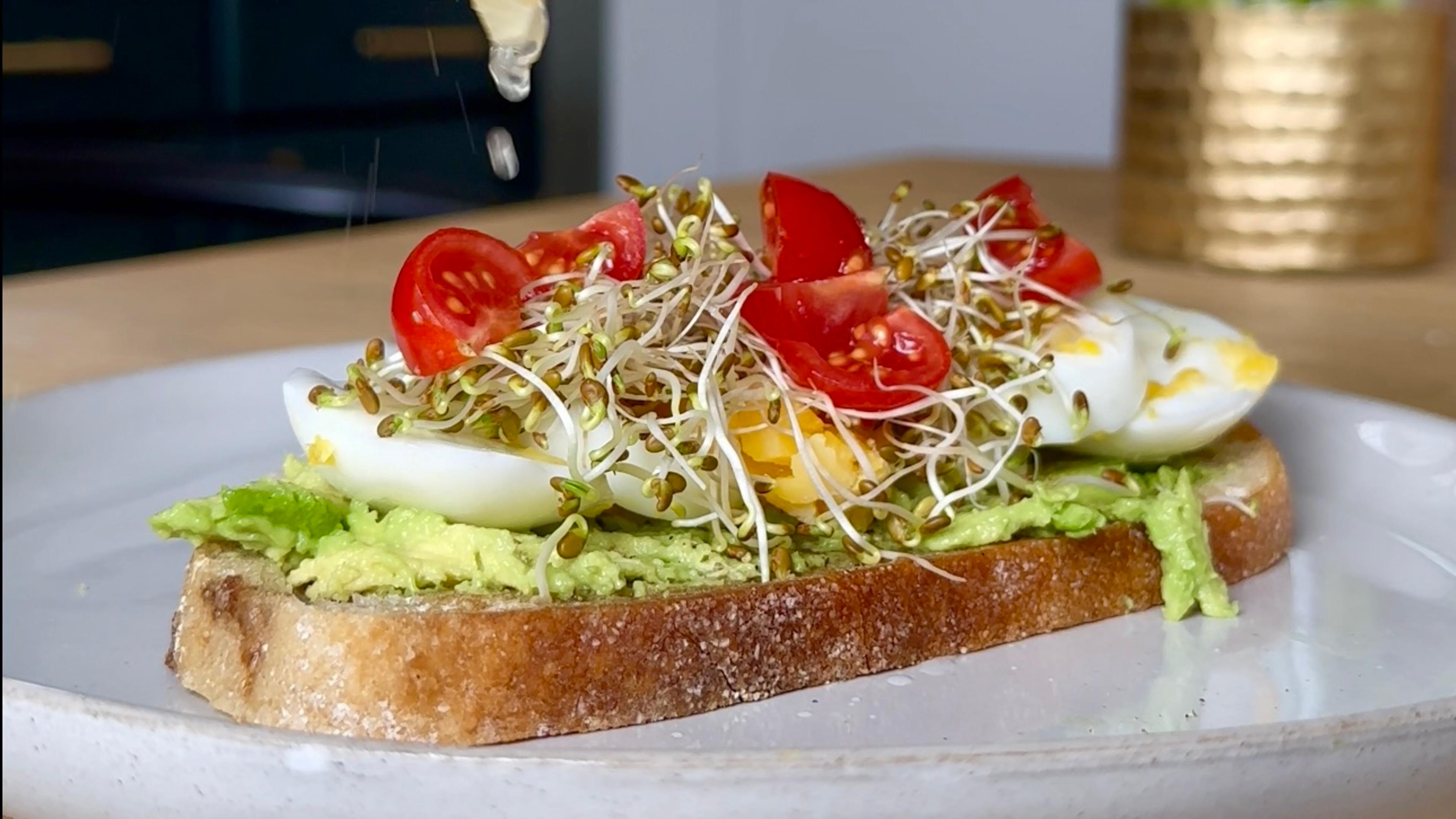 Mashed avocado with sliced eggs, cherry tomatoes and fresh sprouts.