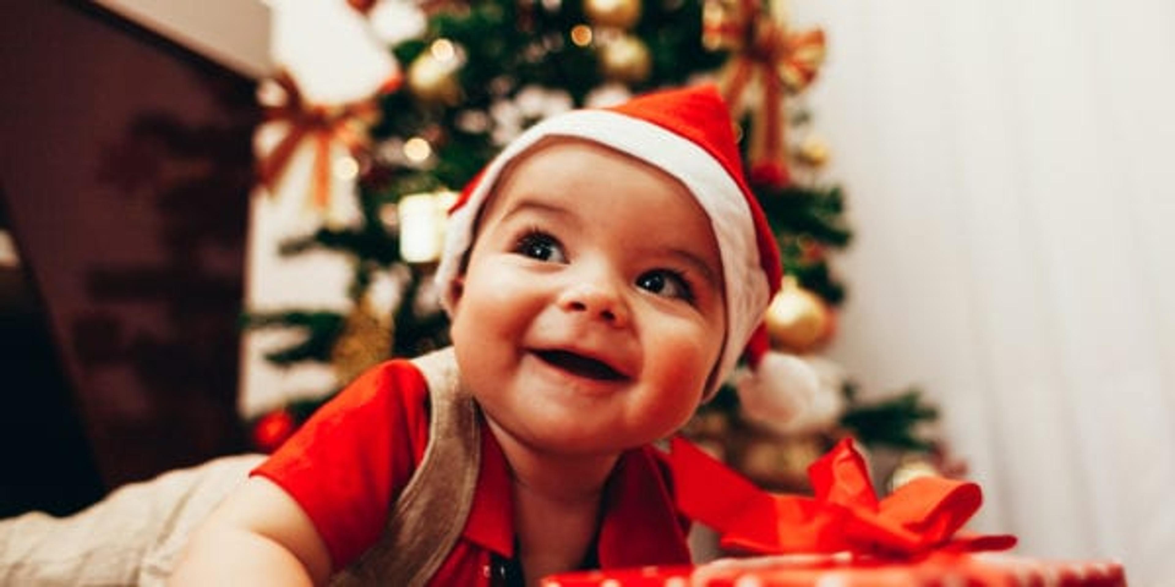 Baby playing with gift box on the living room floor over christmas tree lights on background