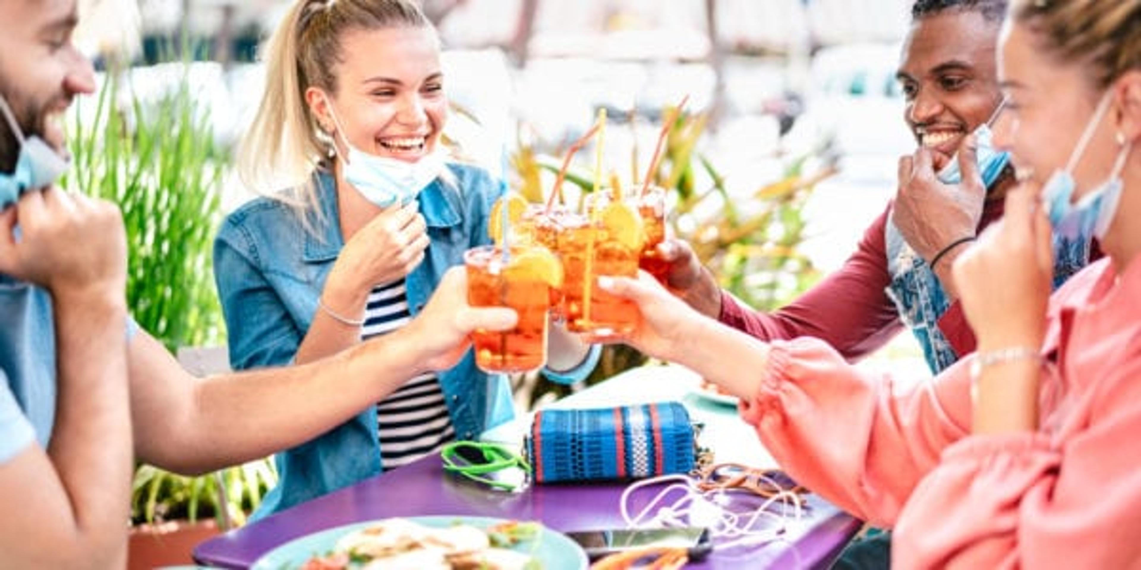 Friends drinking spritz at cocktail bar with face masks - New normal friendship concept with happy people having fun together toasting drinks at restaurant - Bright filter with focus on left woman