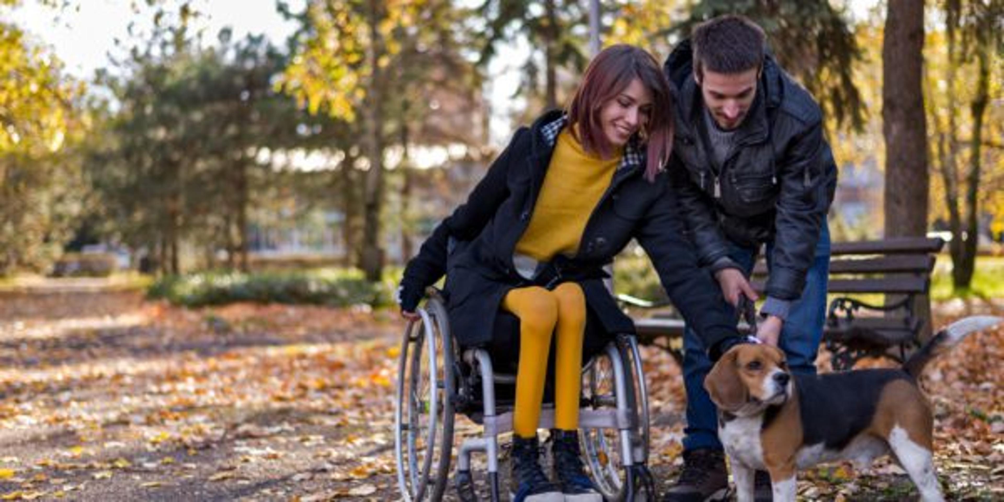 Disabled girl with boyfriend playing with dog in the park in autumn