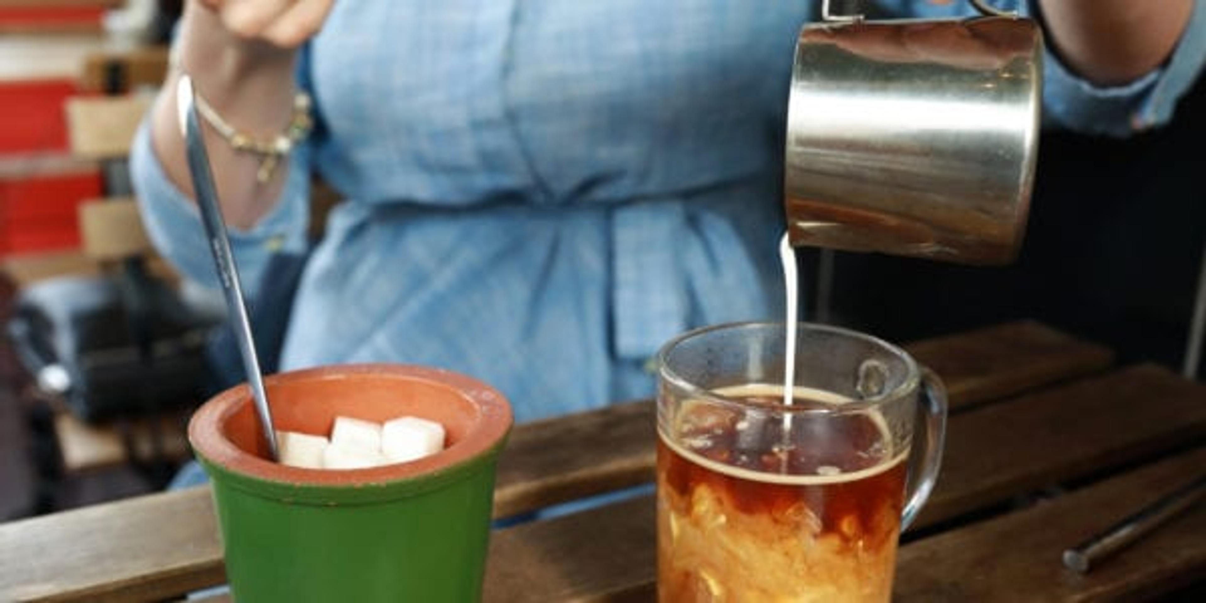 Woman pouring cream into coffee mug in restaurant