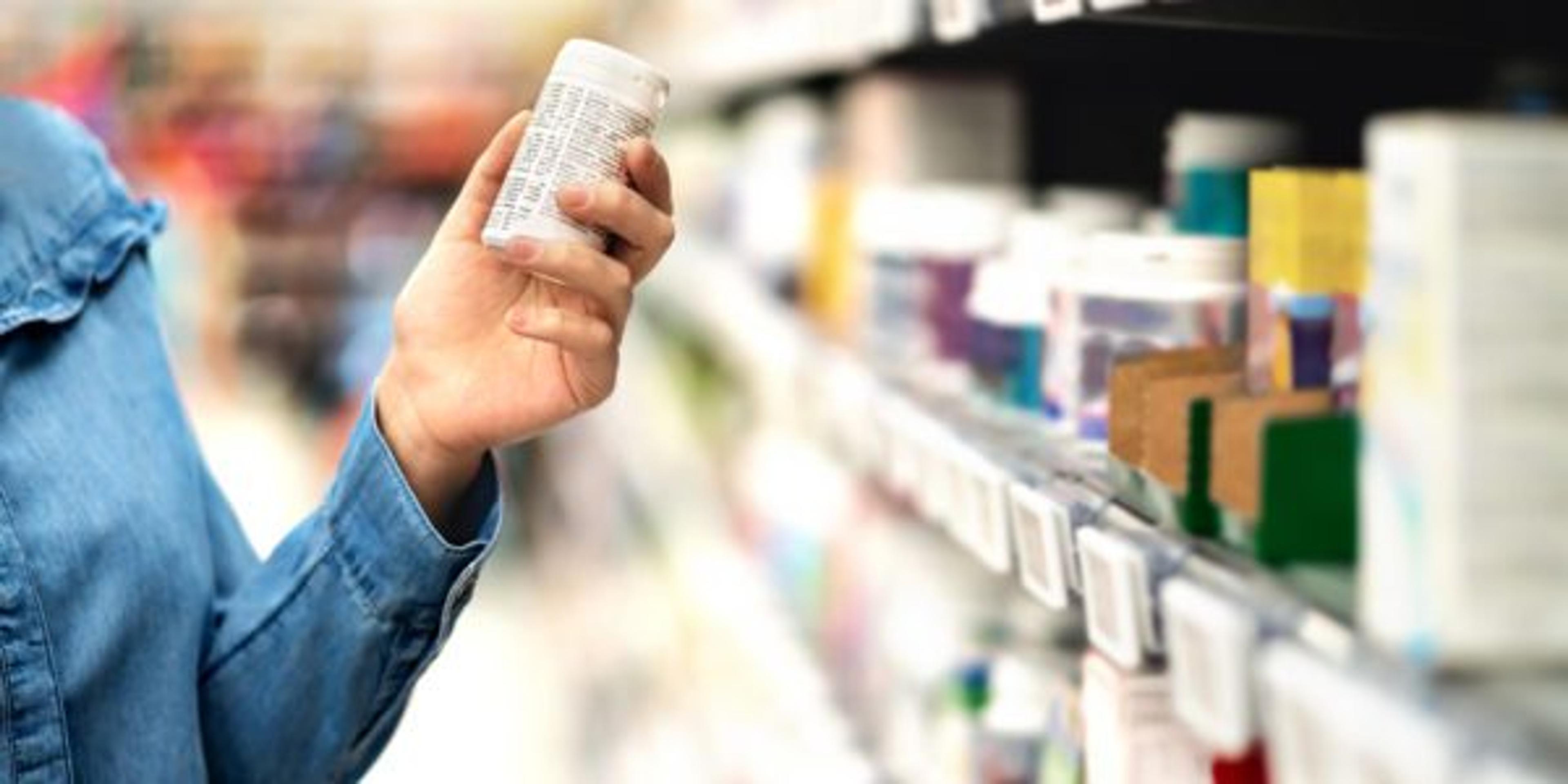 Customer in pharmacy holding medicine bottle. Woman reading the label text about medical information or side effects in drug store. Patient shopping pills for migraine or flu.