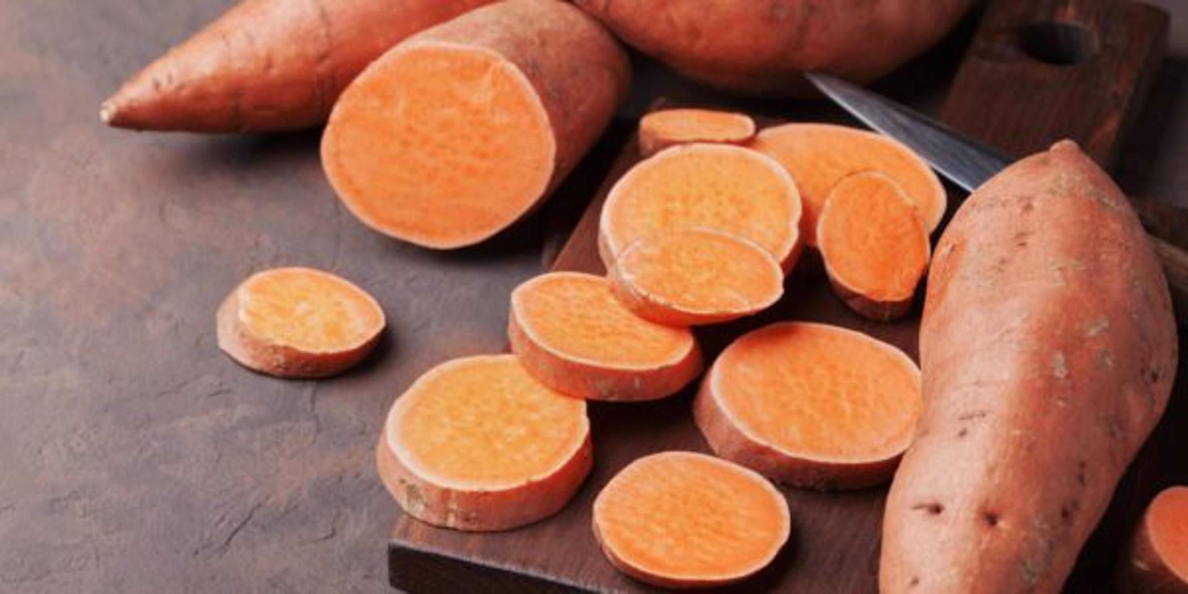 Organic sweet potatoes whole and sliced on wooden kitchen board.