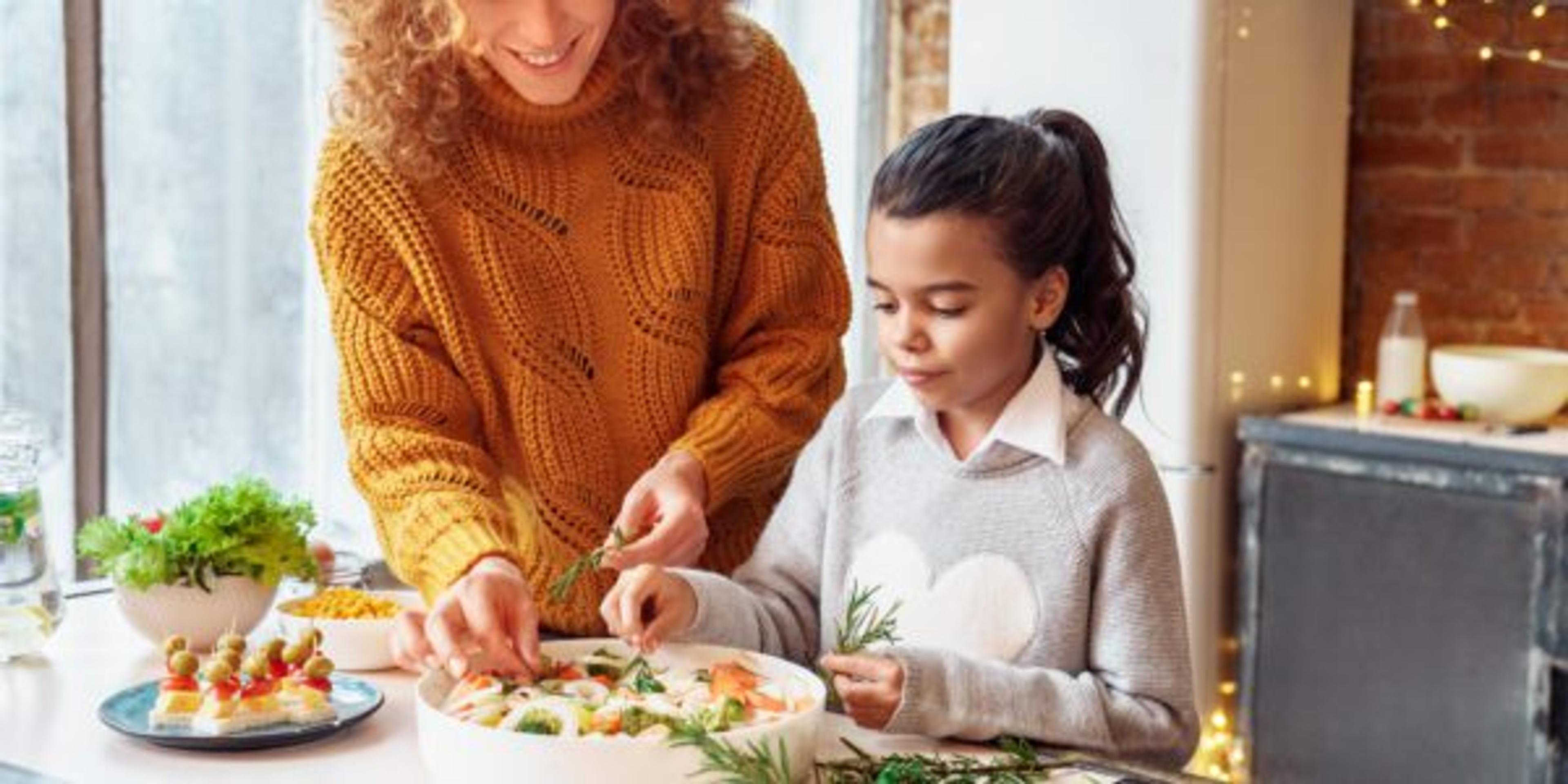 Happy curly woman and a girl niece making healthy vegan food for family feasting