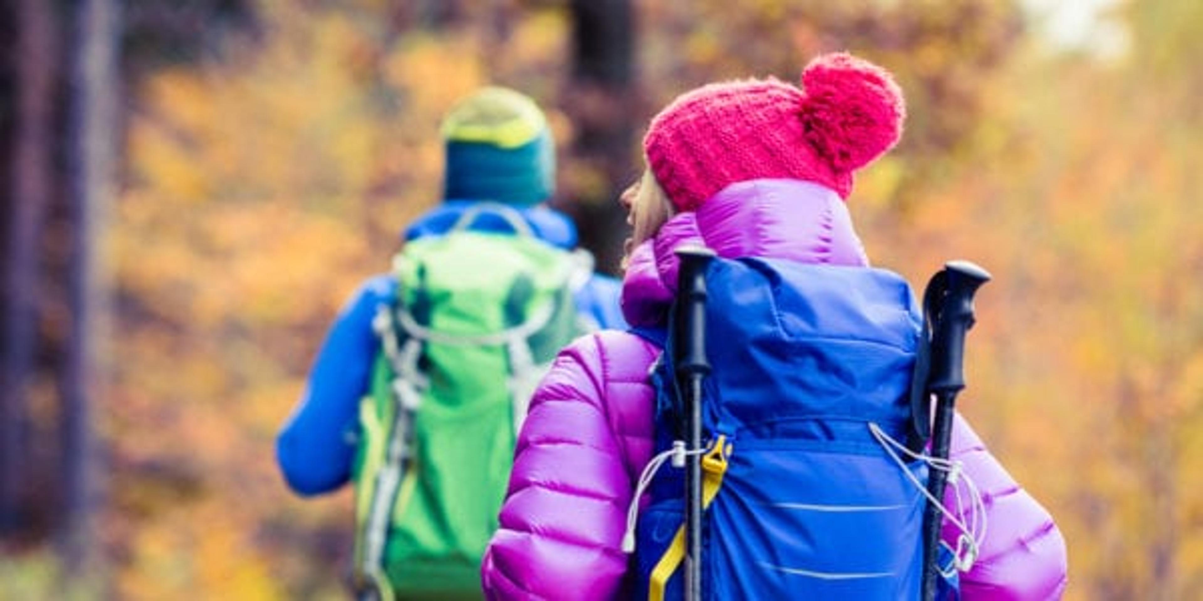 Man and woman couple hikers trekking in yellow autumn woods and mountains. Young people walking on trek trail with backpacks, healthy lifestyle adventure, camping on hiking trip, Poland.