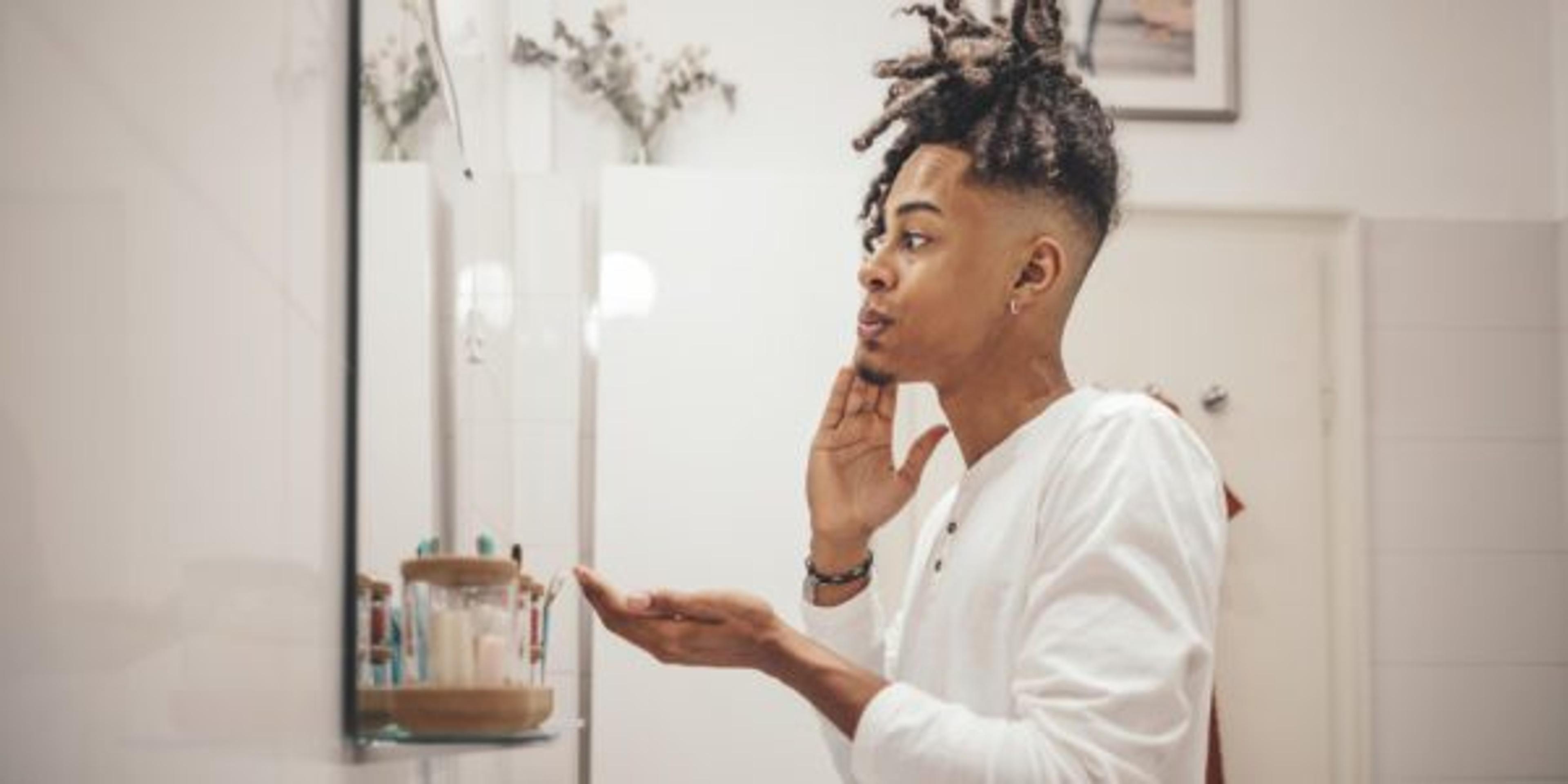 At home - young man engaging in self-care by taking care of his skin in the bathroom