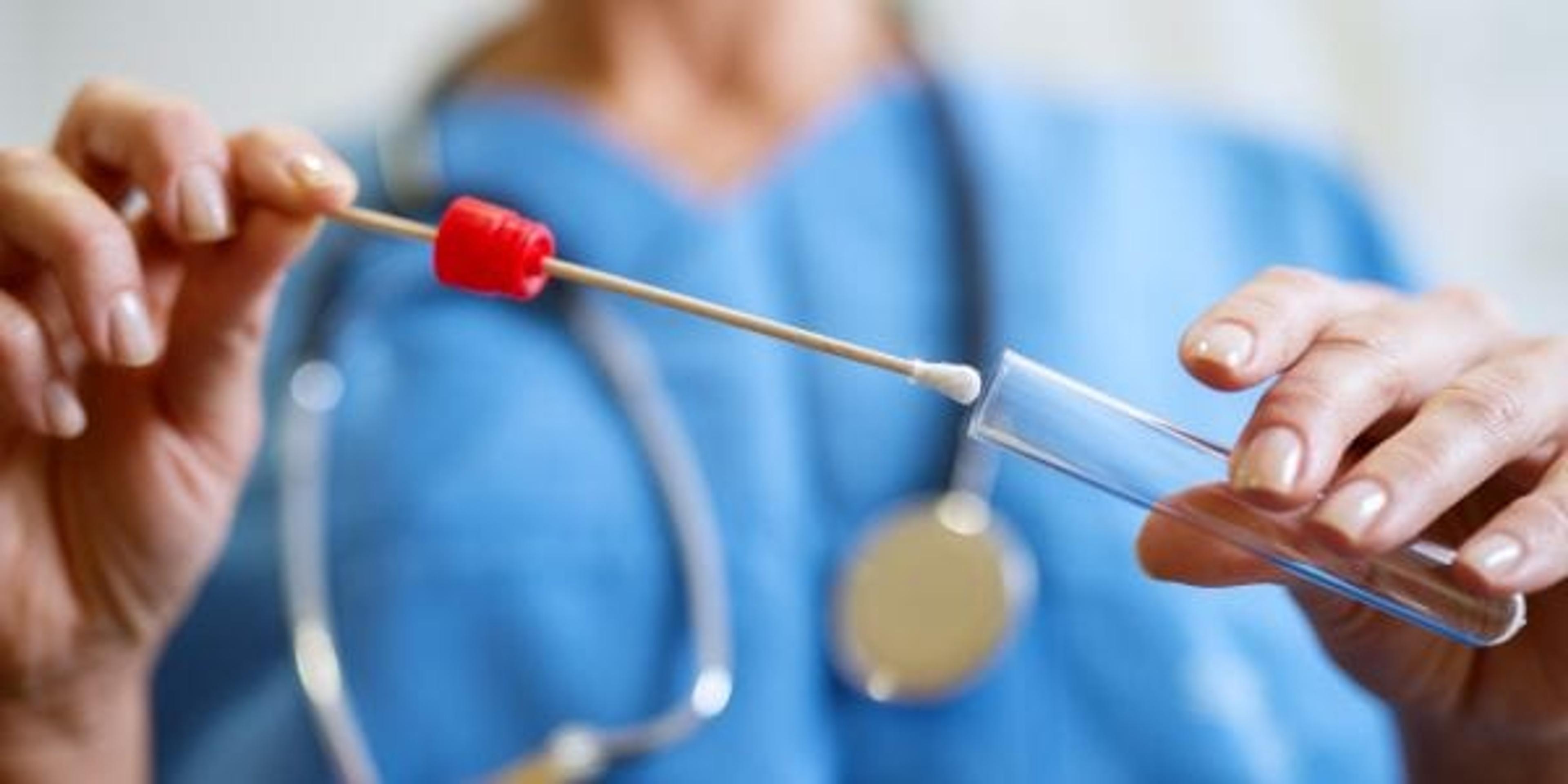 Close up of nurse placing a swab into a vial.