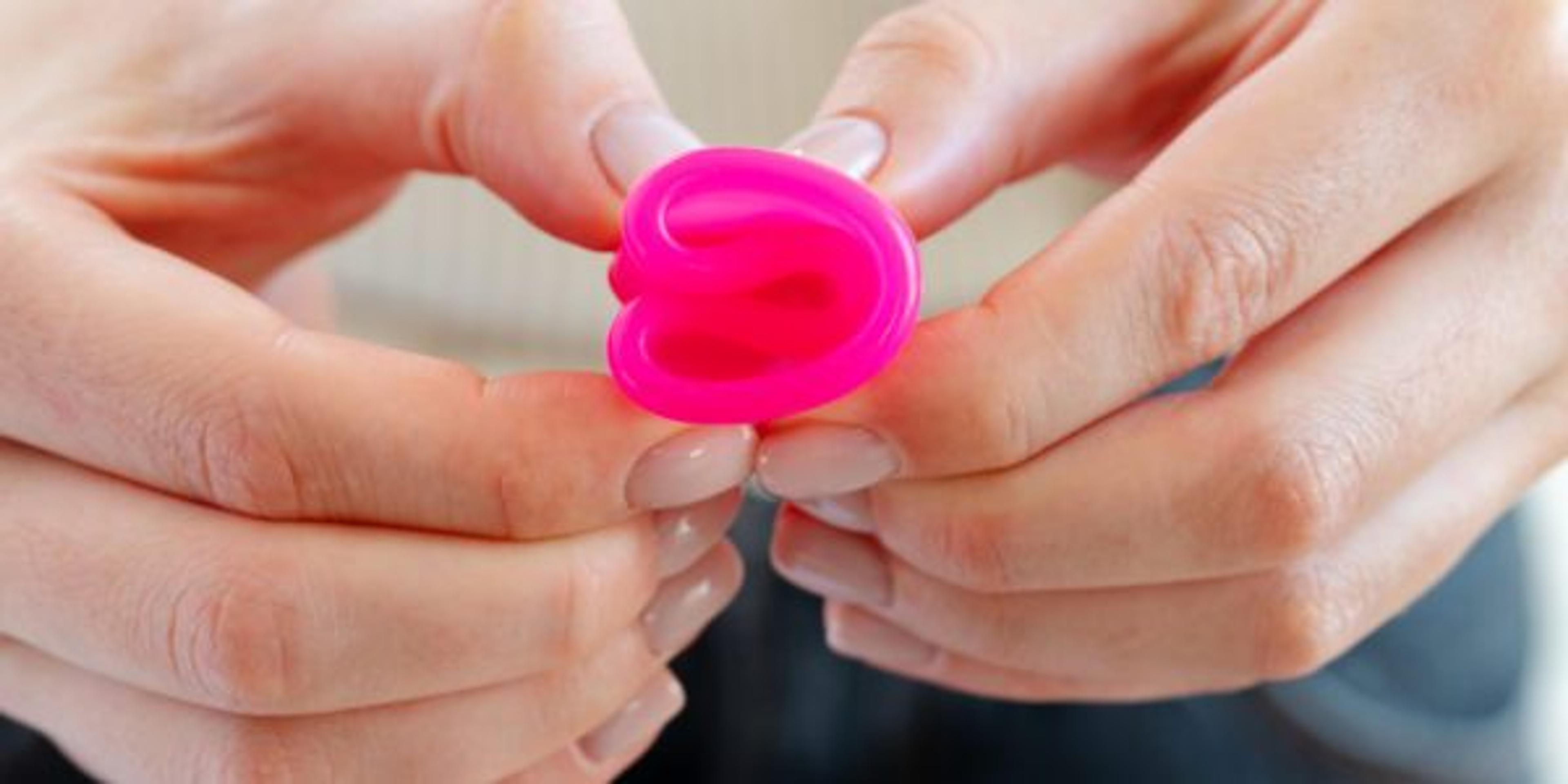 Woman in white sweater holding pink menstrual cup in hands close up