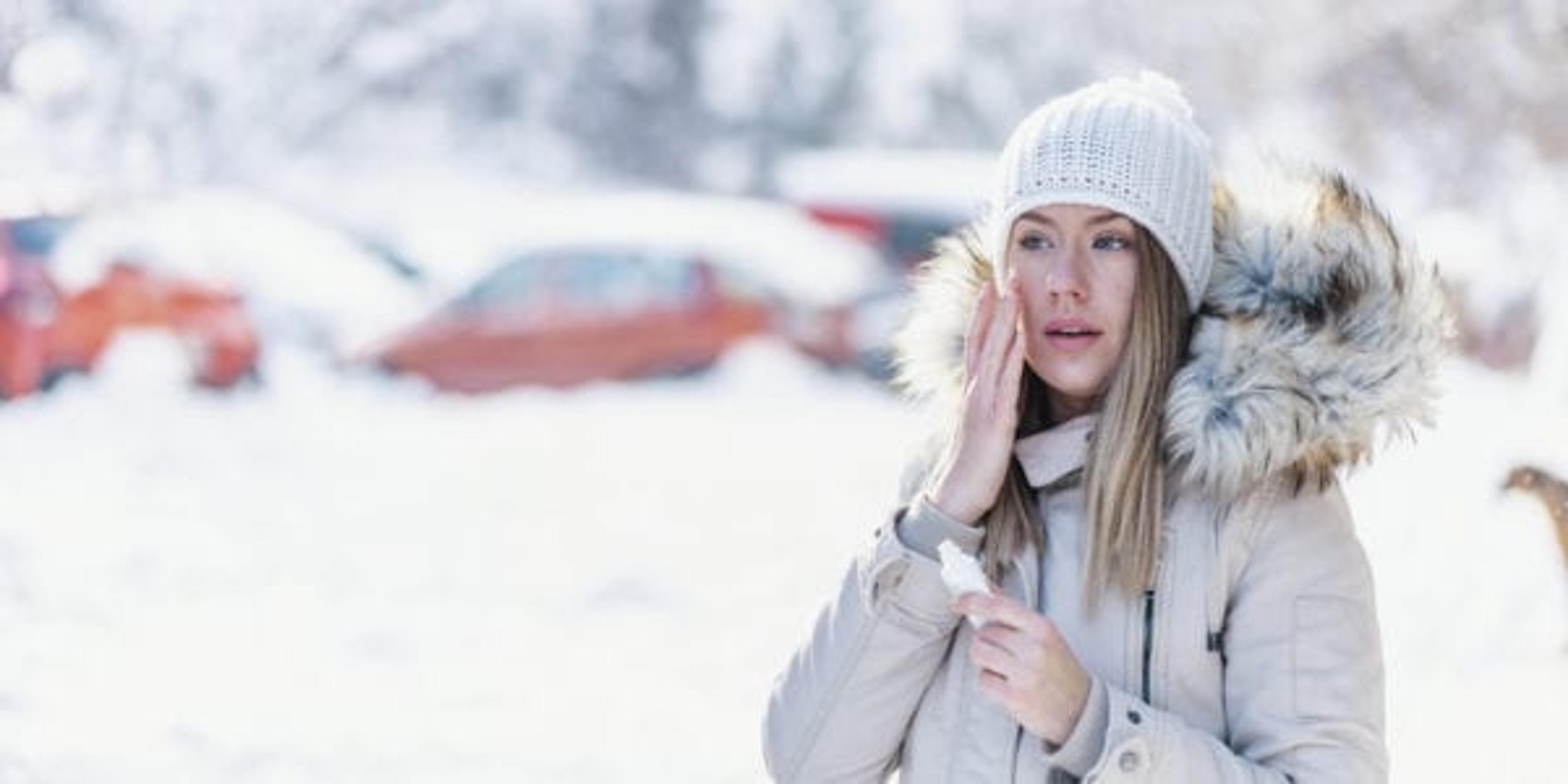 Portrait of a beautiful woman in snow with application of the protective cream in winter. Portrait of a beauty happy lady applying facial moisturiser cream in winter