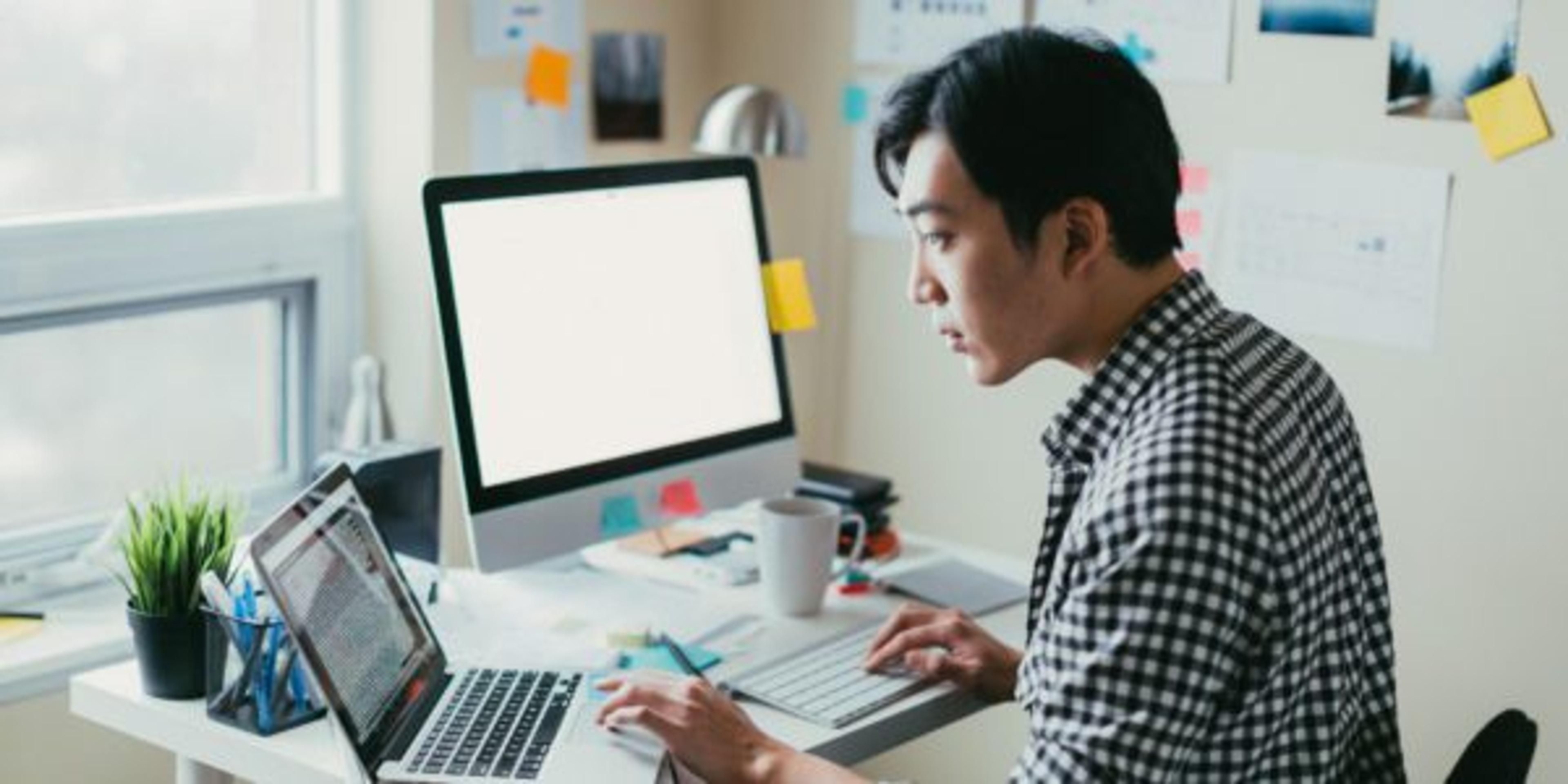 Man looking at computer code on a laptop while working from his small office.