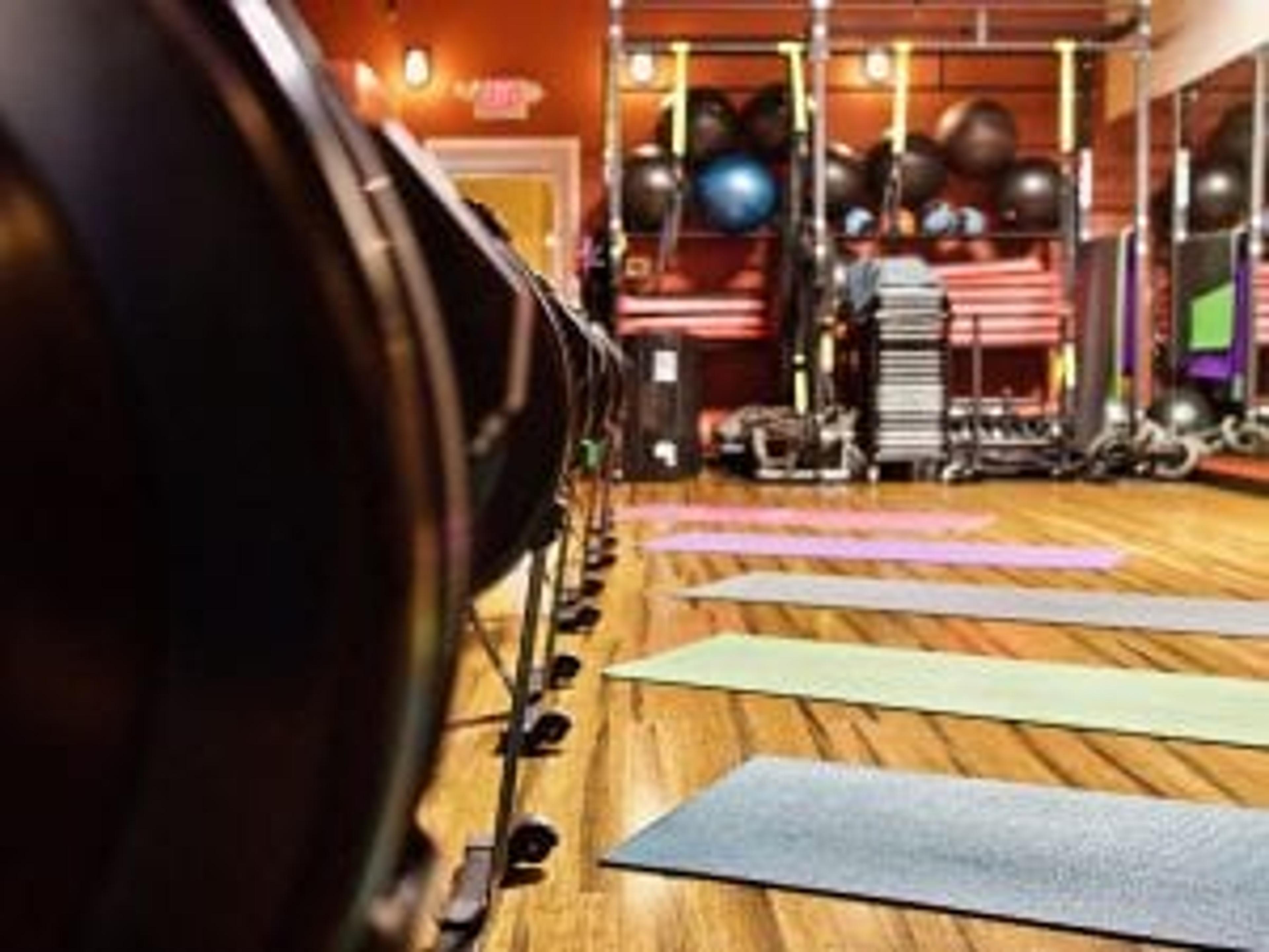 A line of rowing machines faces yoga mats placed on a gym studio floor. 
