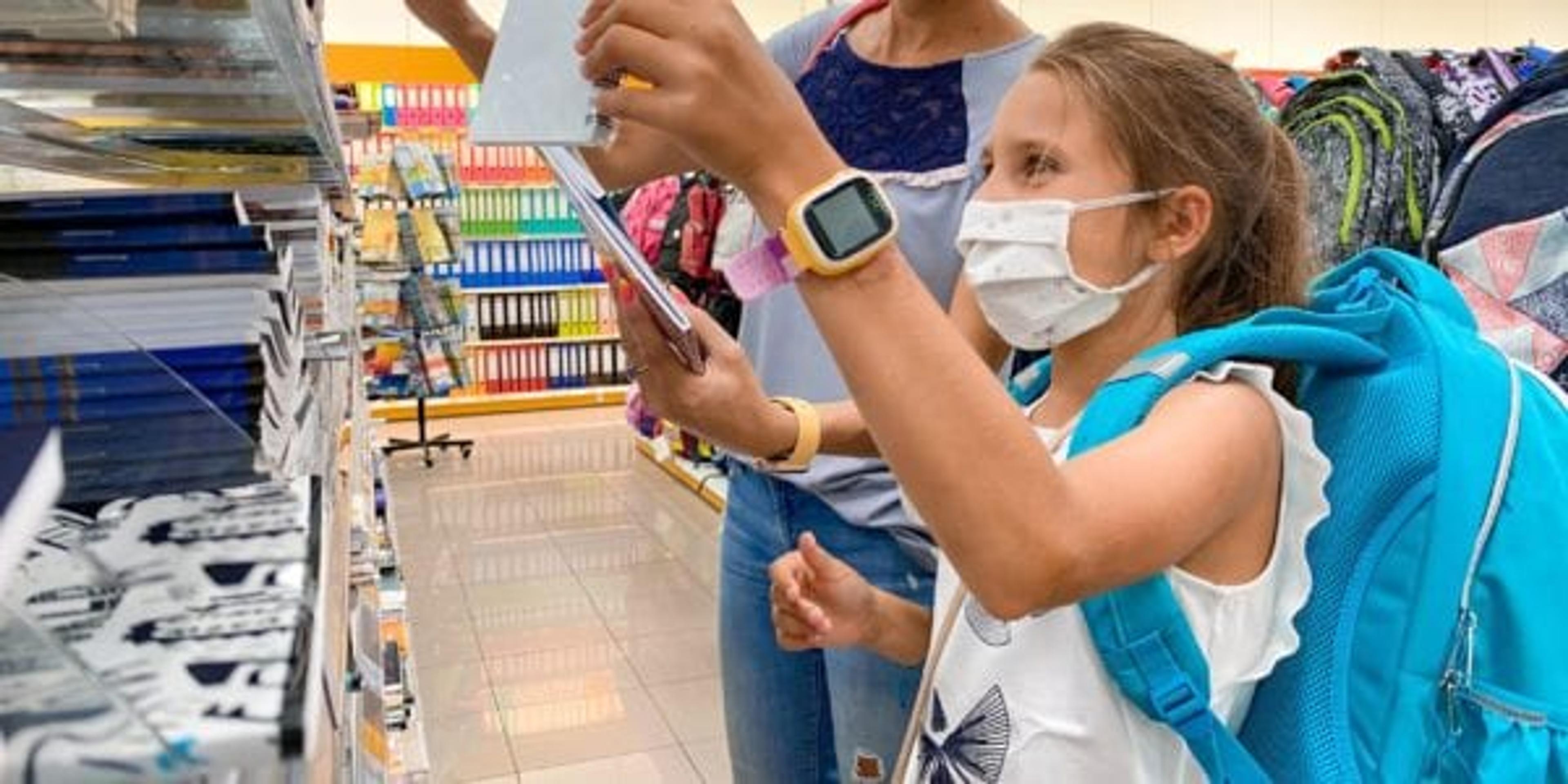Little girl picking out school supplies with her mom, both wearing masks