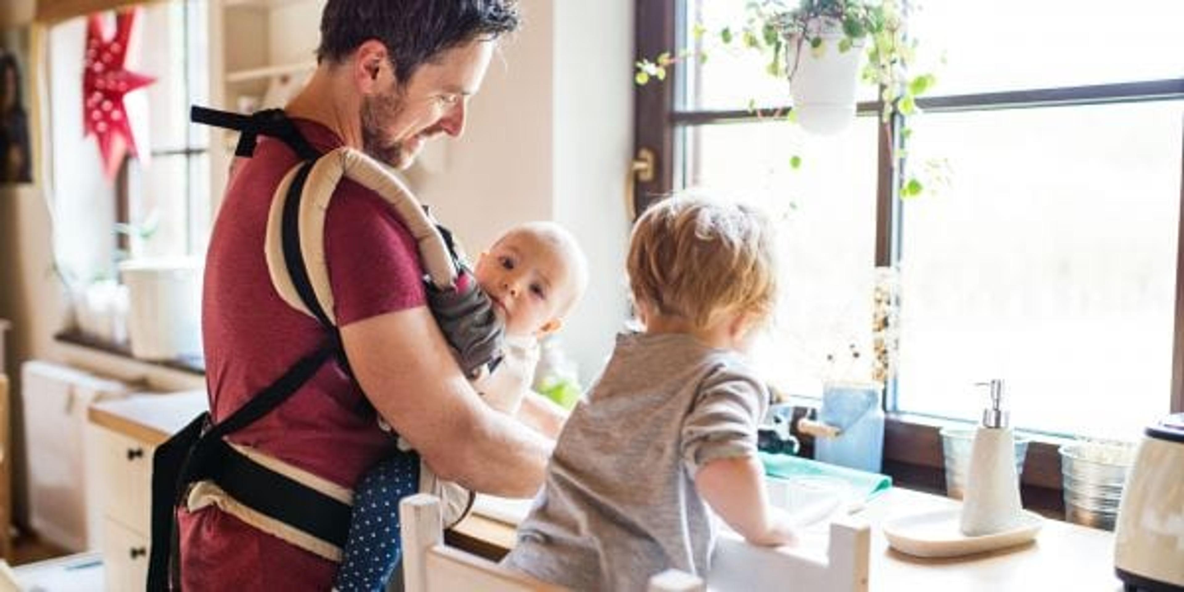 Dad babywearing and helping a toddler with the dishes.