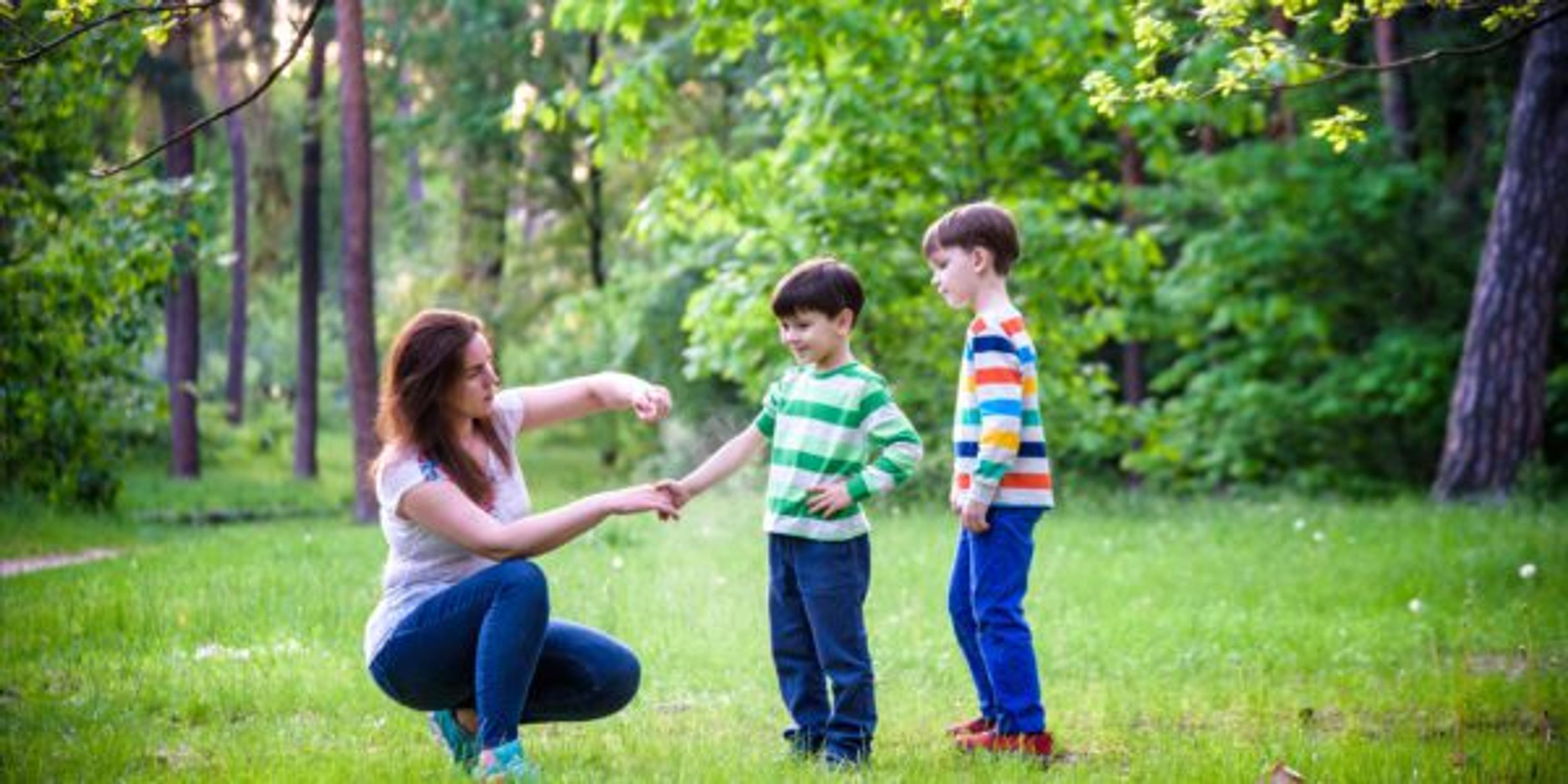 Young woman mother applying insect repellent to her two son before forest hike beautiful summer day or evening. Protecting children from biting insects at summer. Active leisure with kids