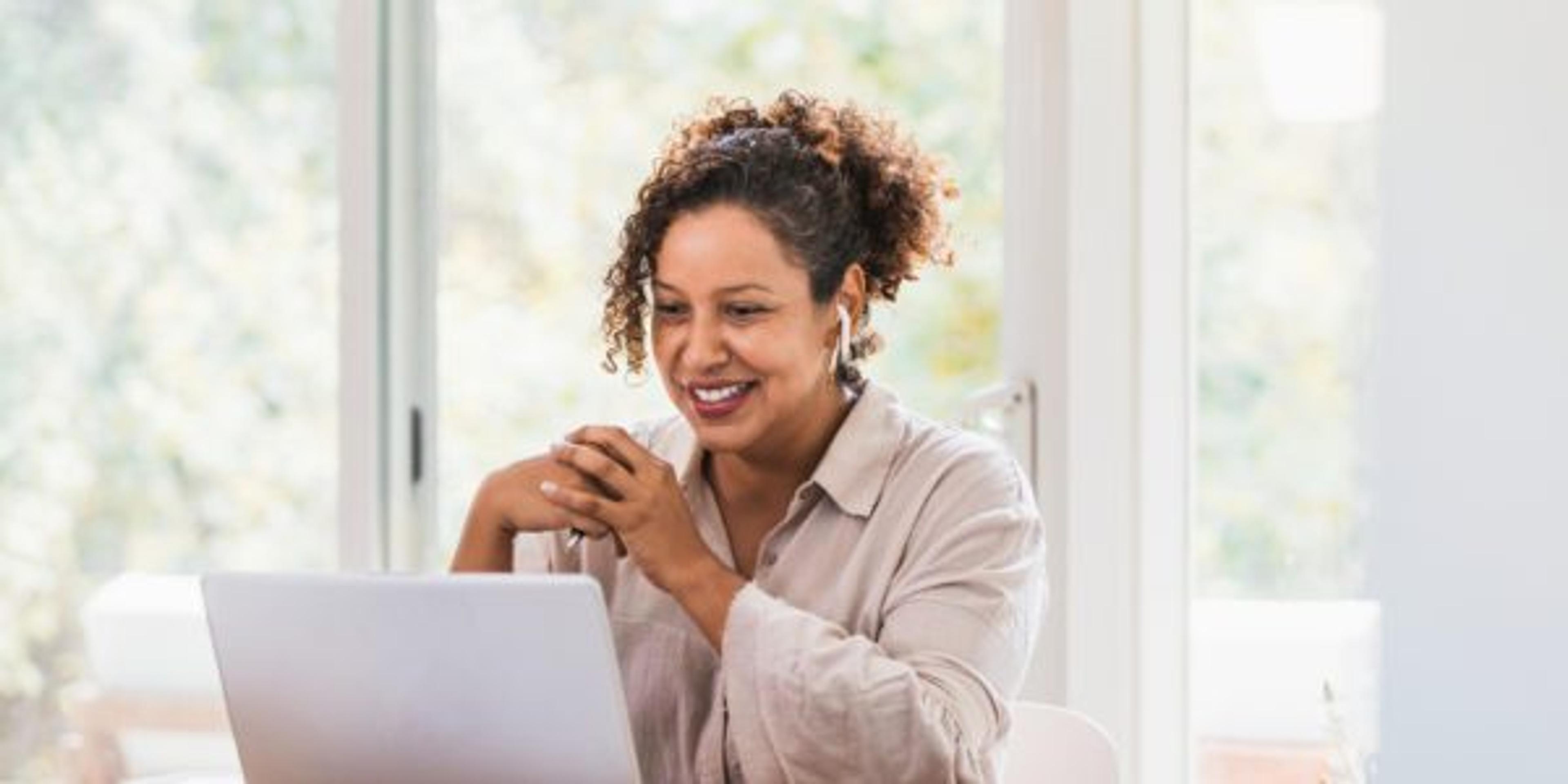 Using laptop and bluetooth earbuds, woman video conferences from home